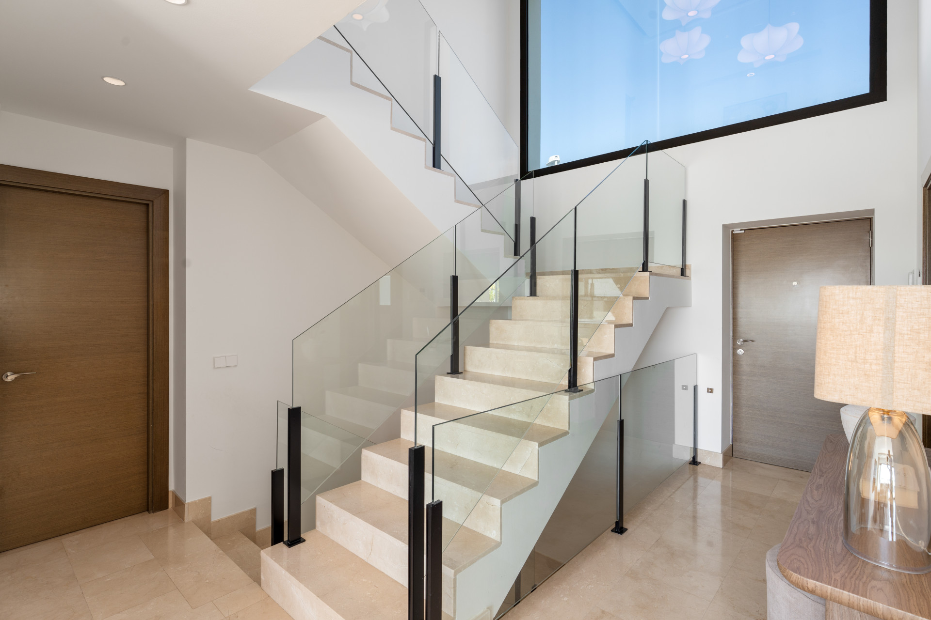 Elegant staircase with glass railing and natural light from overhead.
