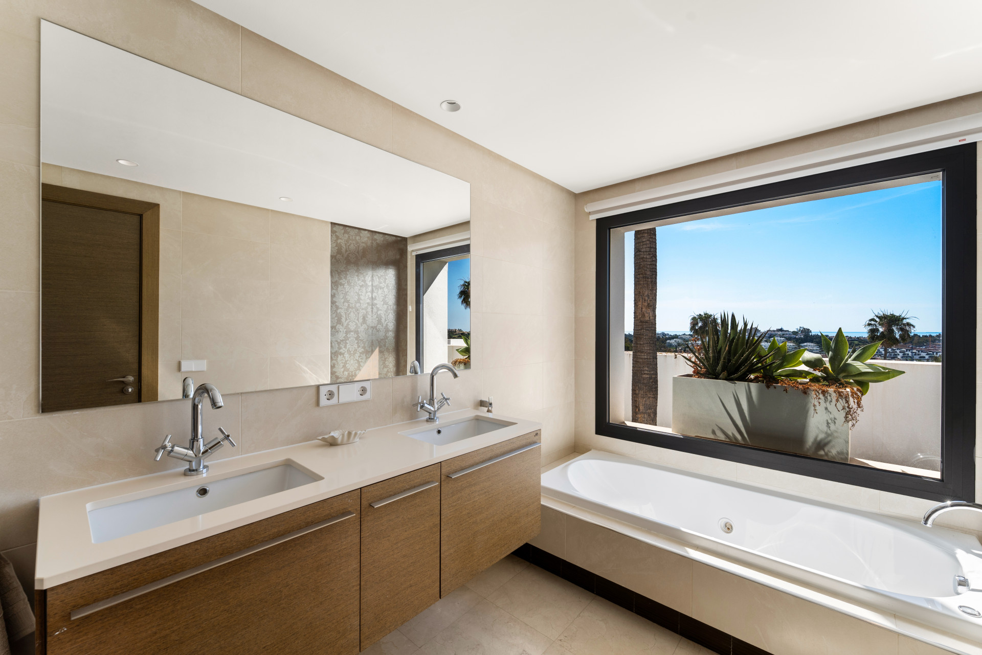 Well-lit bathroom with dual sinks, a bathtub, and a large window with views.