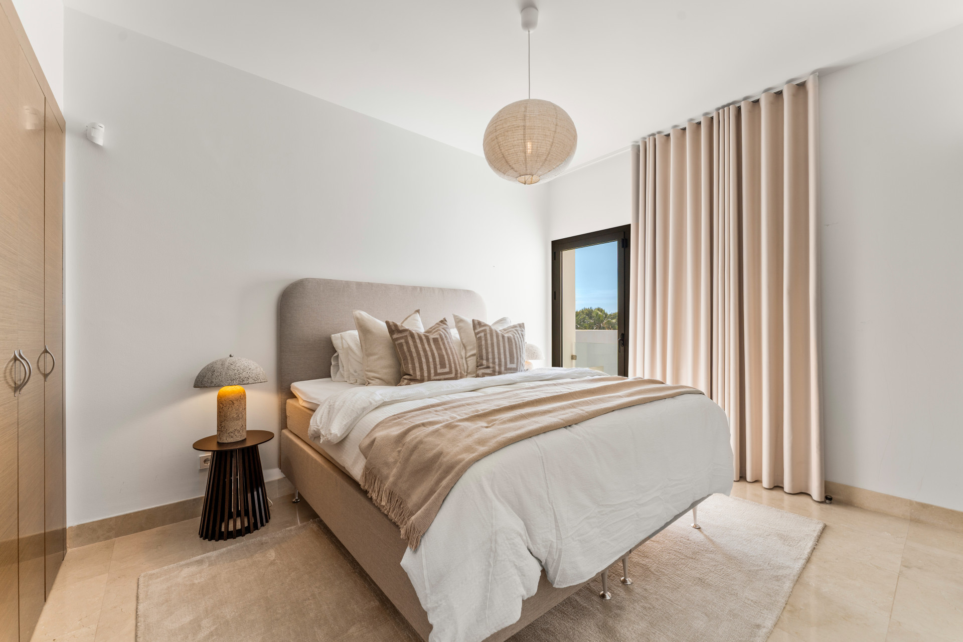 Stylish bedroom with a king-sized bed, light curtains, and a bedside lamp.