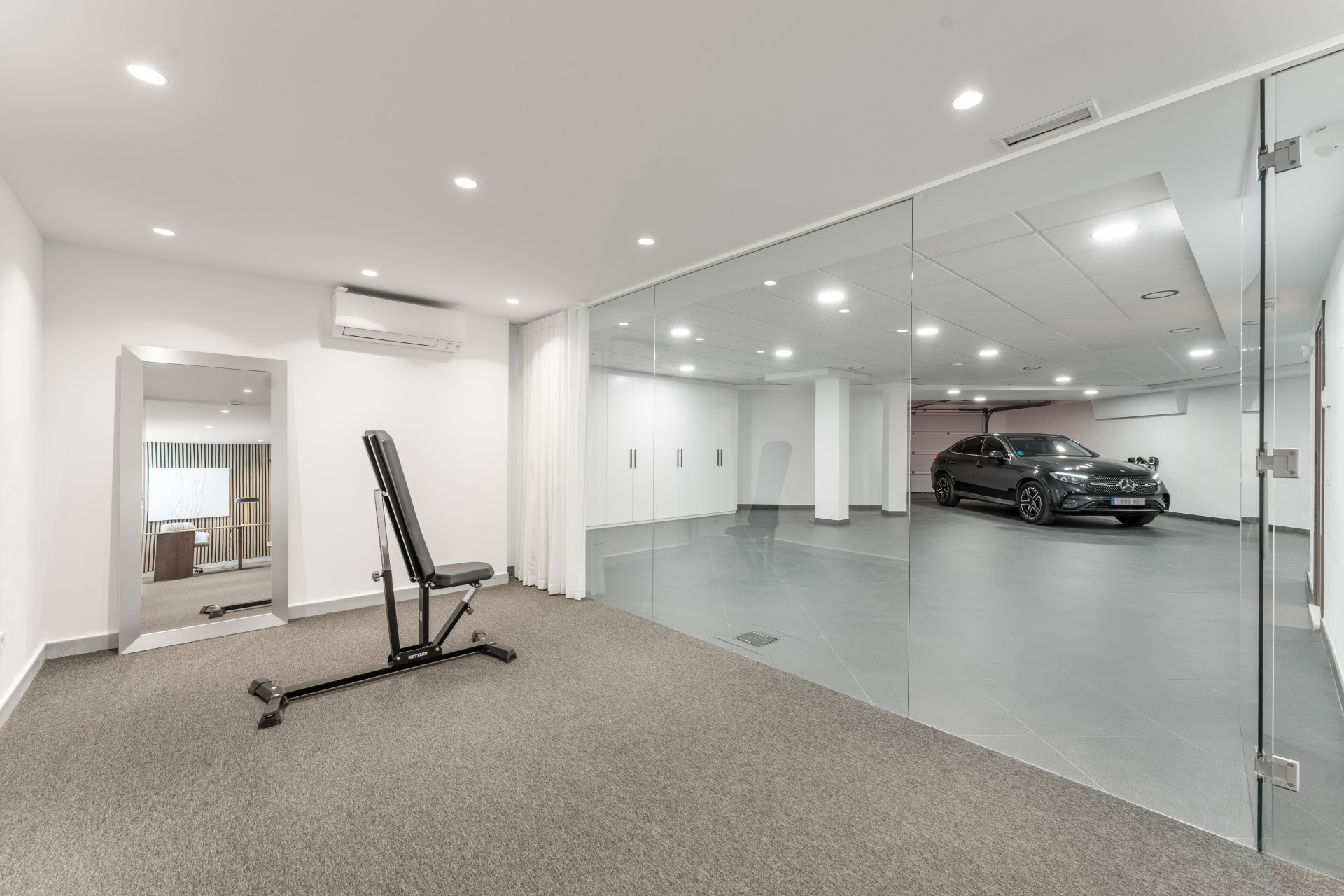 Fitness area with a workout bench and a glass-walled garage showcasing a parked vehicle.