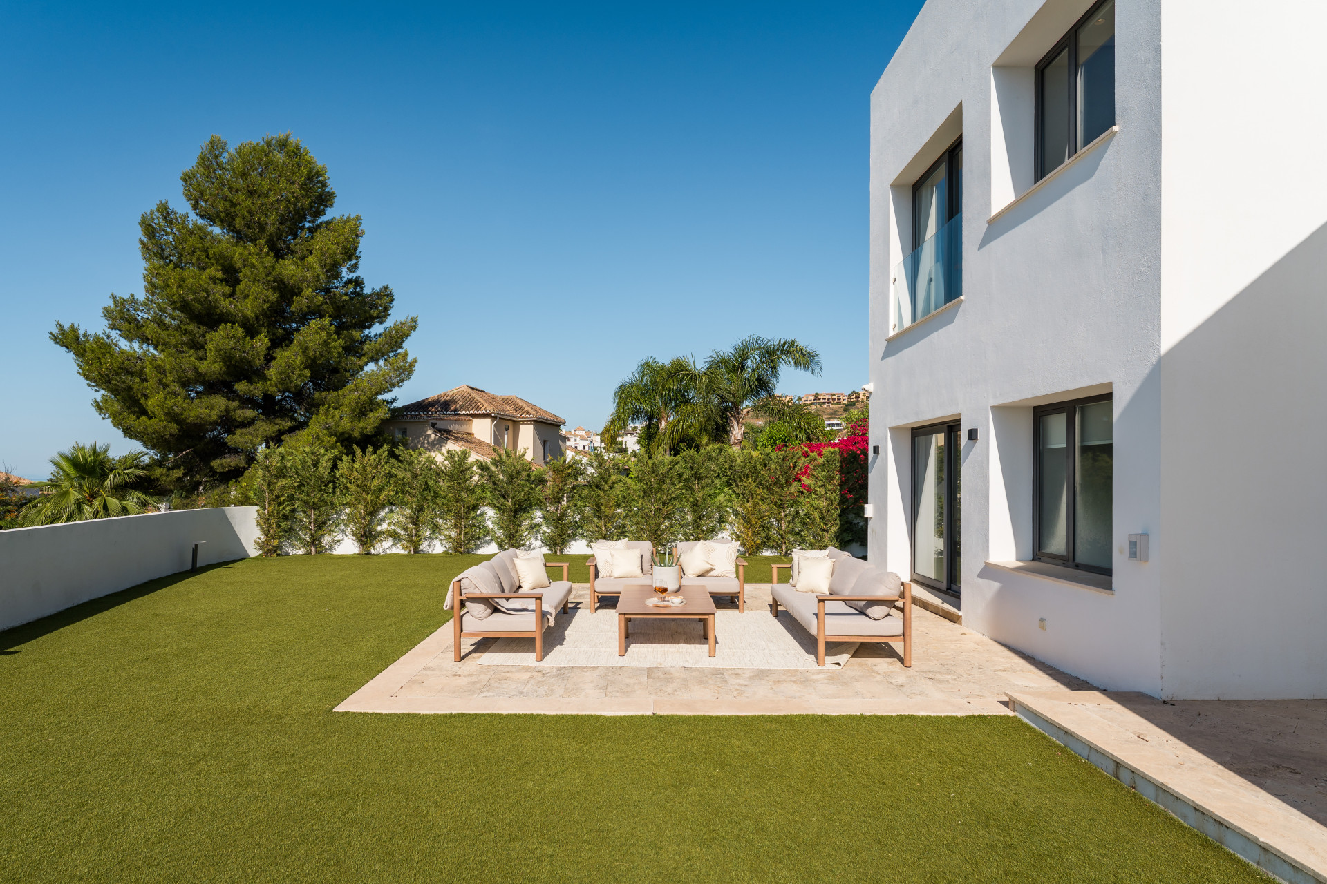 Outdoor seating area with couches and a coffee table on a lawn under clear blue skies.