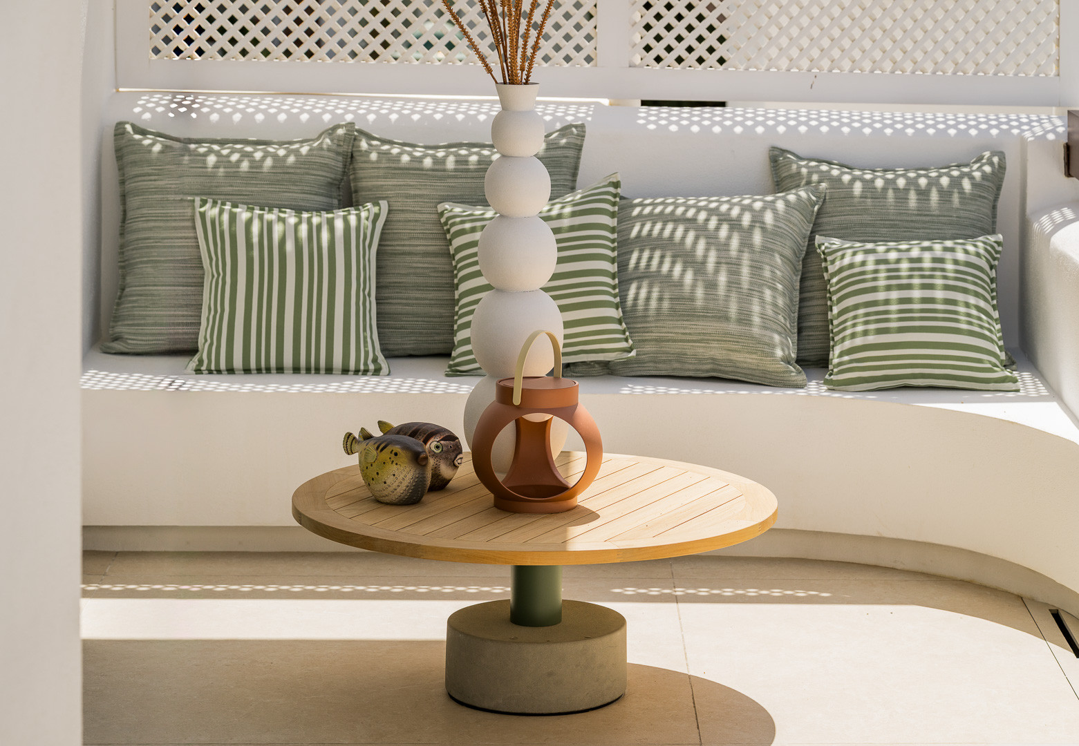 Outdoor lounge area with white built-in seating, green striped cushions, and round wooden coffee table.