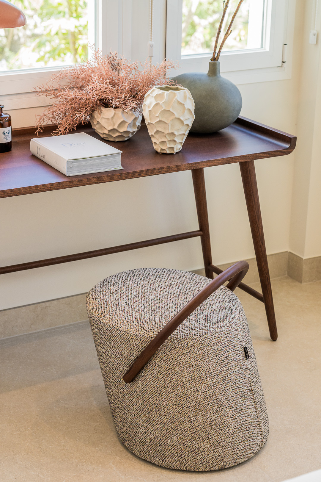 Desk area with a wooden table, decorative vases, a book, and a textured ottoman stool.