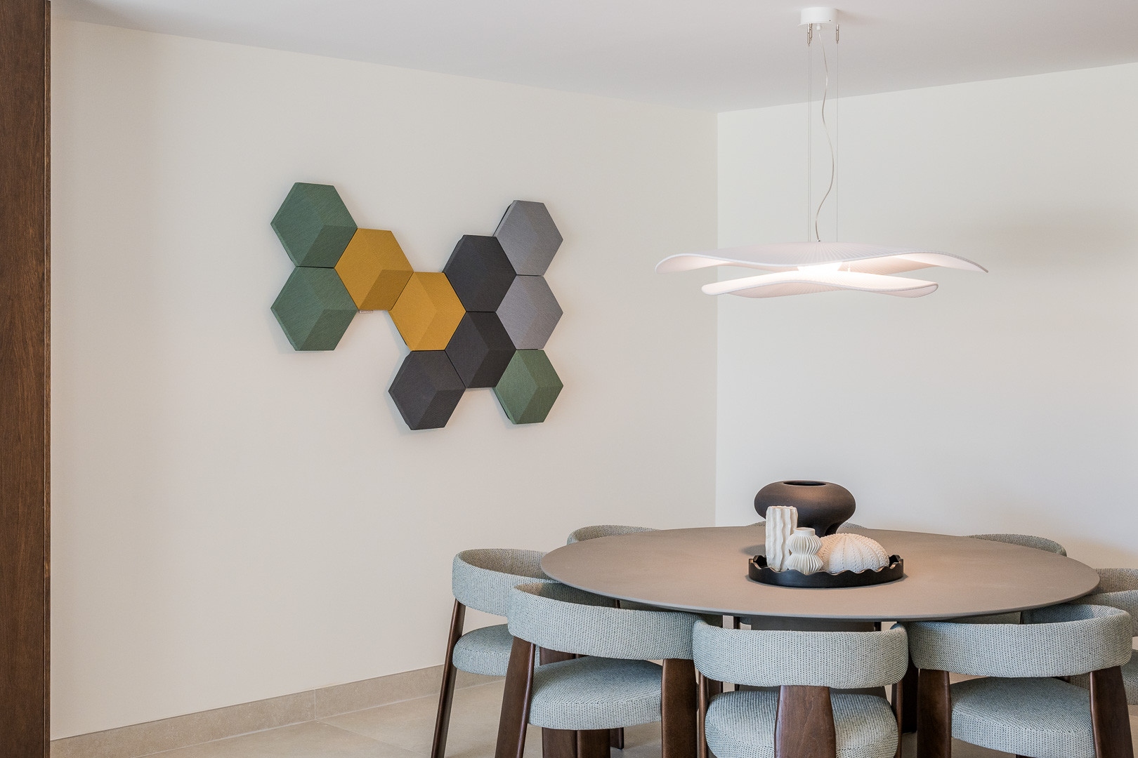 Dining area with a round table, six upholstered chairs, and a geometric wall art piece in shades of green and gray.