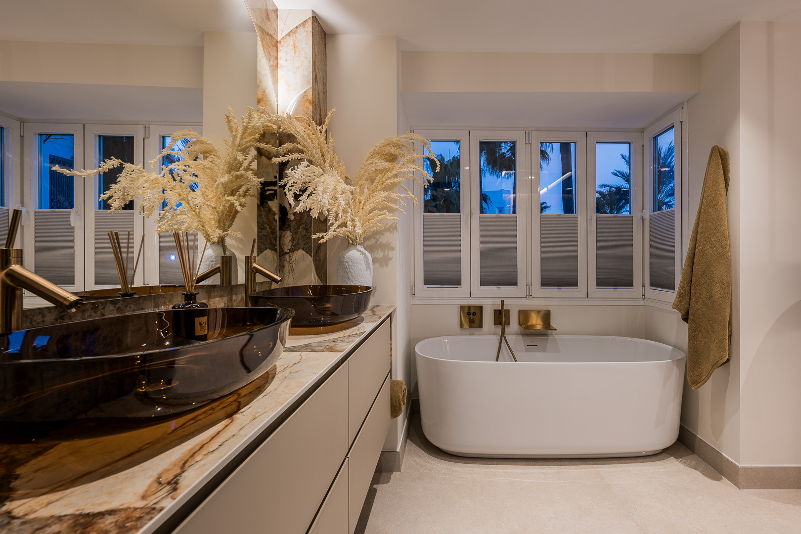 Bathroom with double vessel sinks, a freestanding tub, and small windows with white blinds.