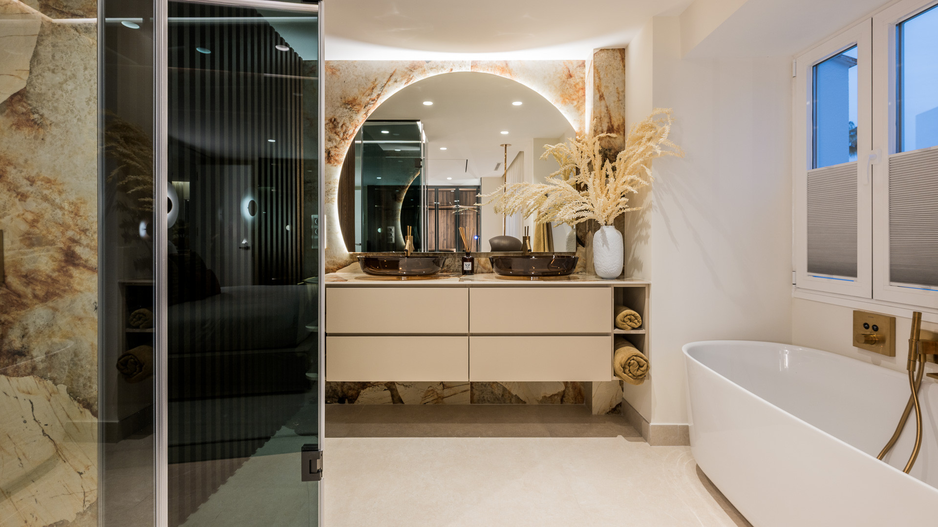 Bathroom with double vanity, circular mirror, freestanding bathtub, and glass shower enclosure.
