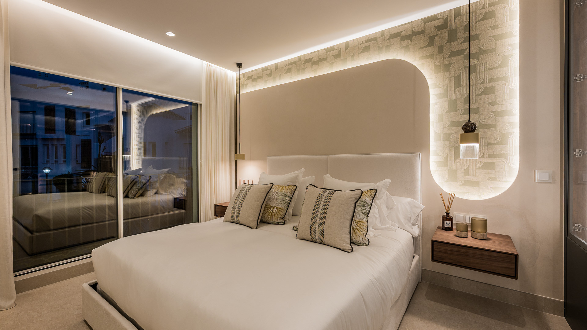 Bedroom with a large bed, patterned headboard wall with cove lighting, and a glass sliding door.