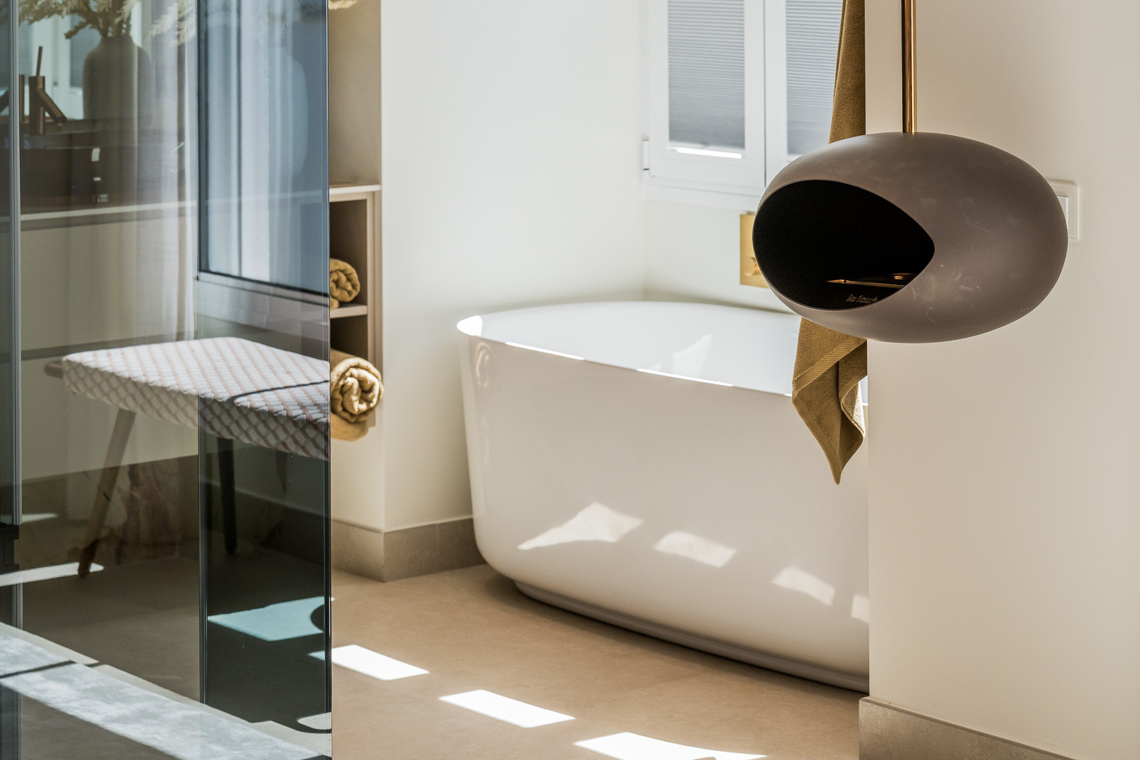 Bathroom with a freestanding tub and a contemporary wall-mounted fireplace. Sunlit floor.