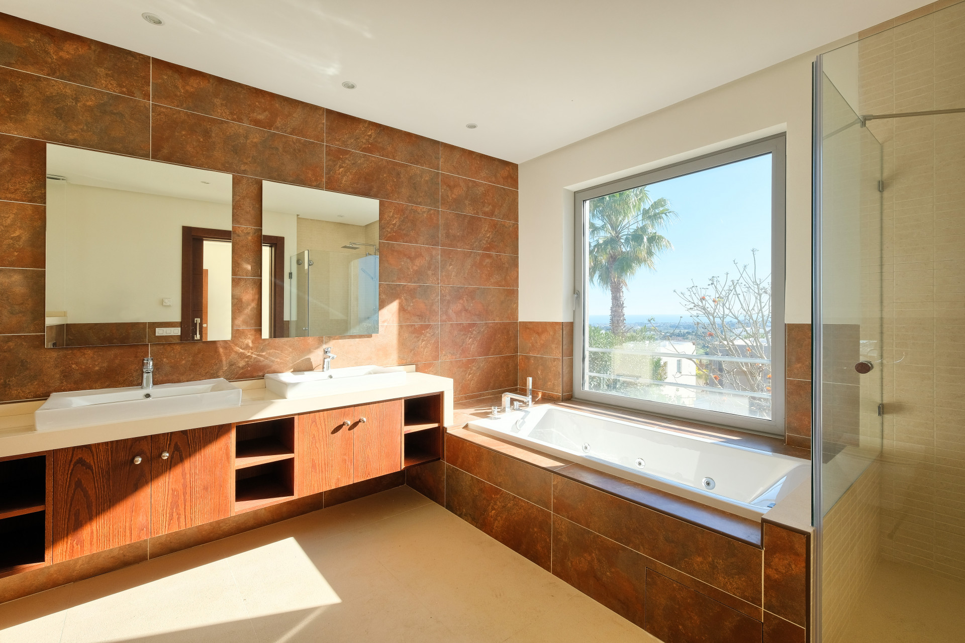Bathroom with brown tile walls, large window, built-in bathtub, and a glass-enclosed shower on the right.