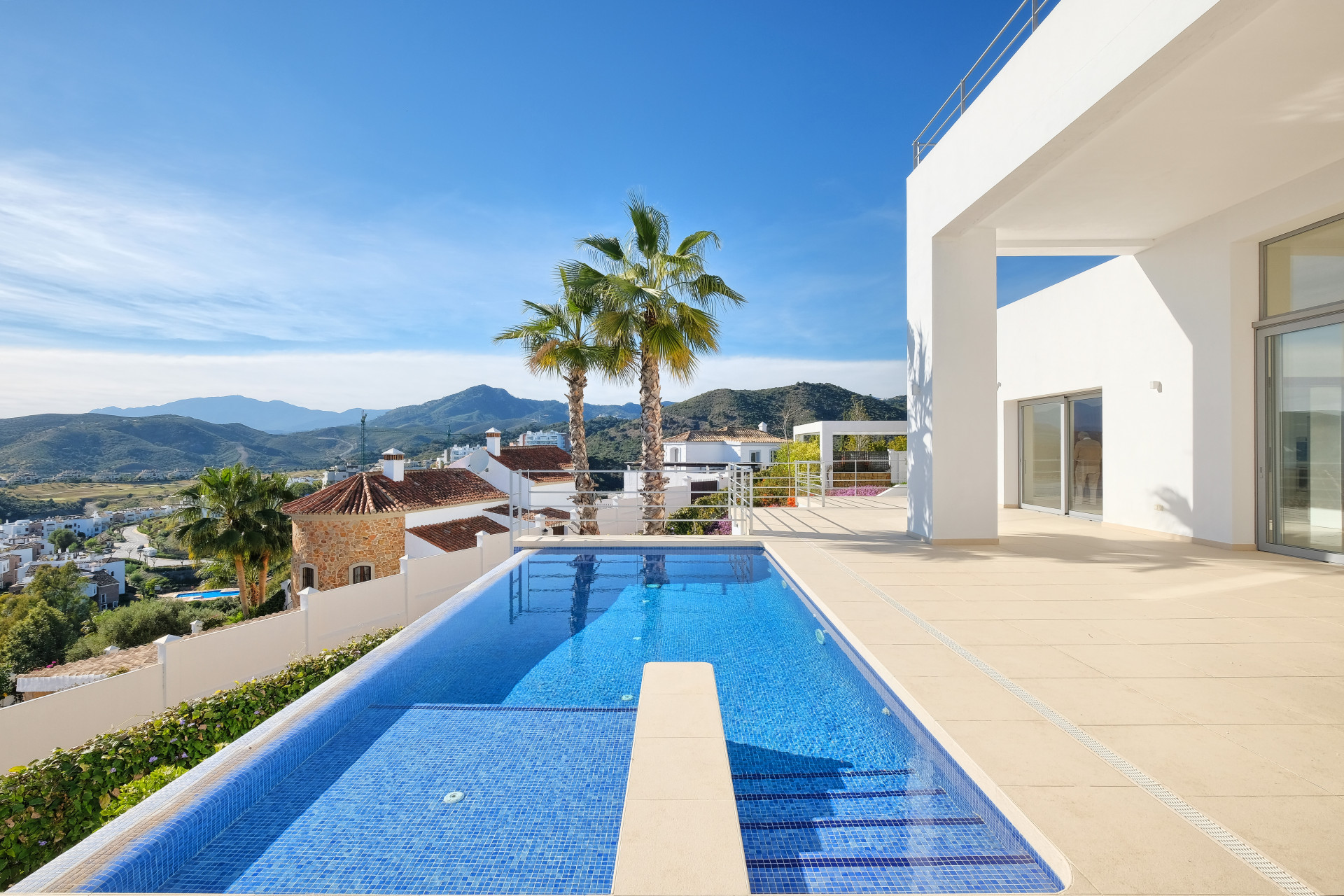 Outdoor pool with blue tiles, diving platform, and distant mountains under a clear sky.