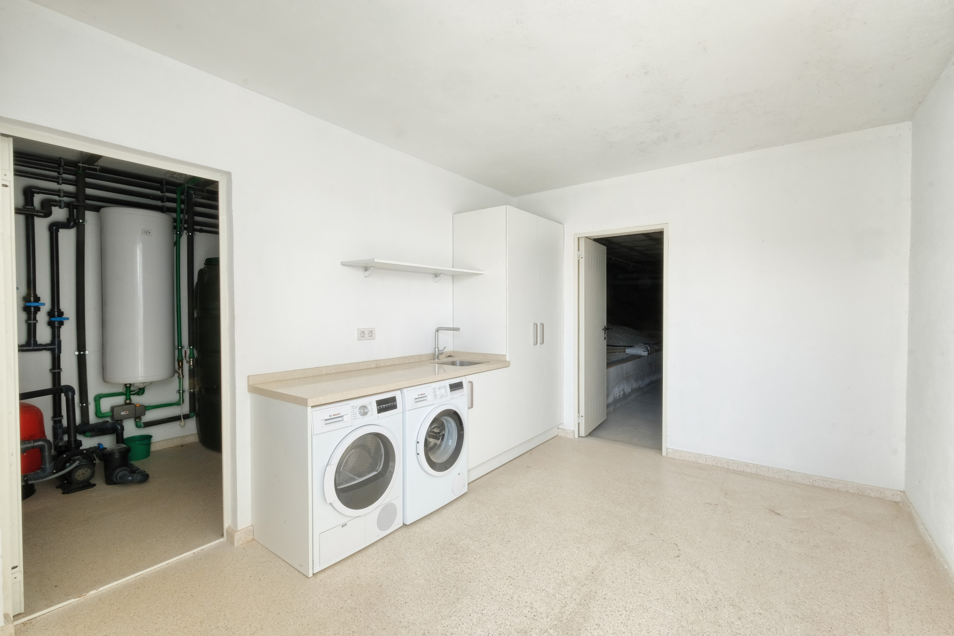 Laundry room with stacked washer and dryer, sink, storage, and utility area visible through an open doorway.