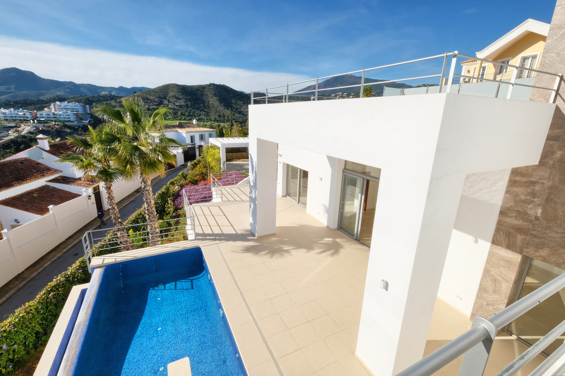 Outdoor terrace with small blue swimming pool, white railing, and view of residential area and mountains.
