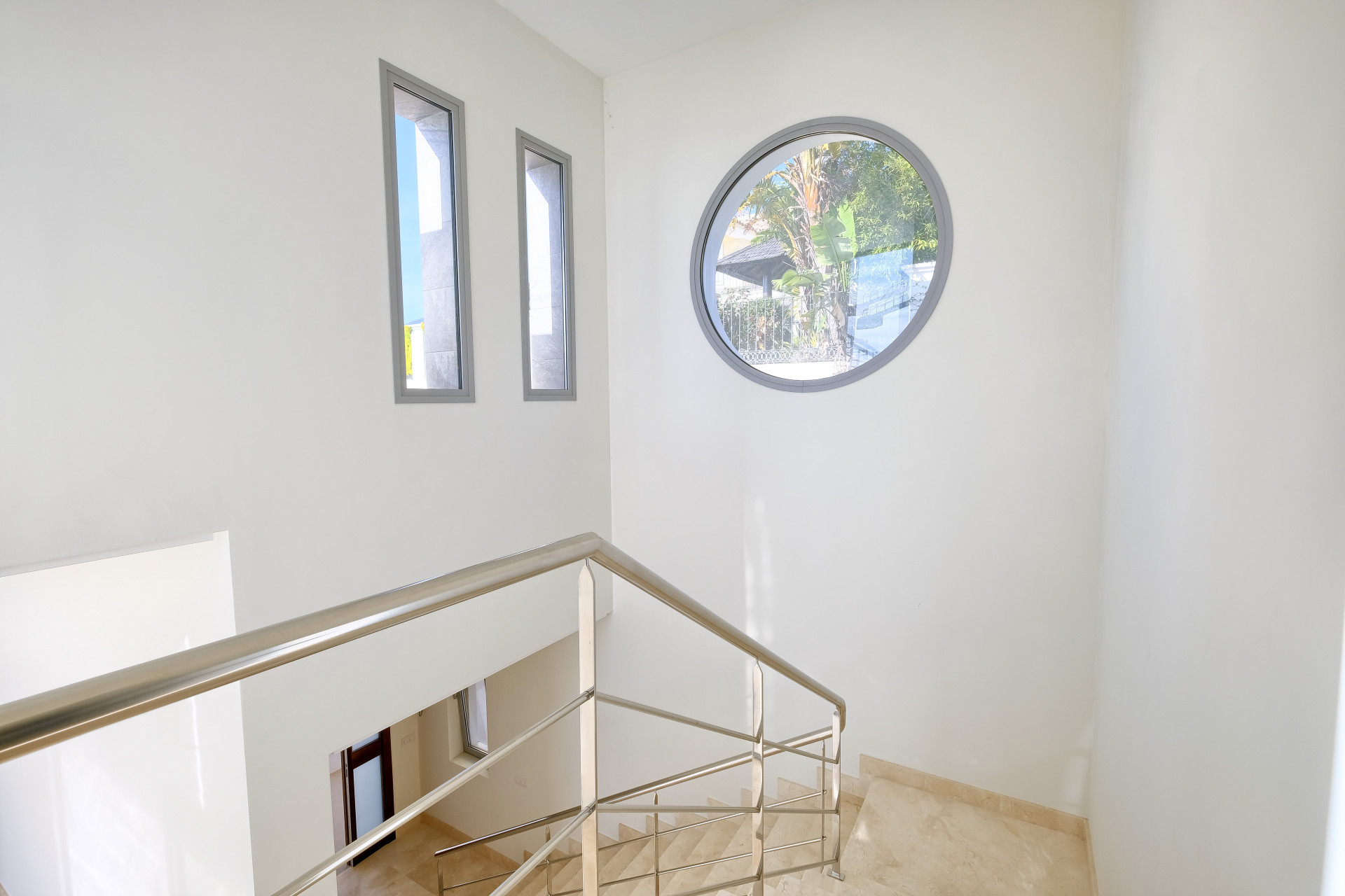 Stairwell with a modern metal railing, a large round window, and two vertical rectangular windows.