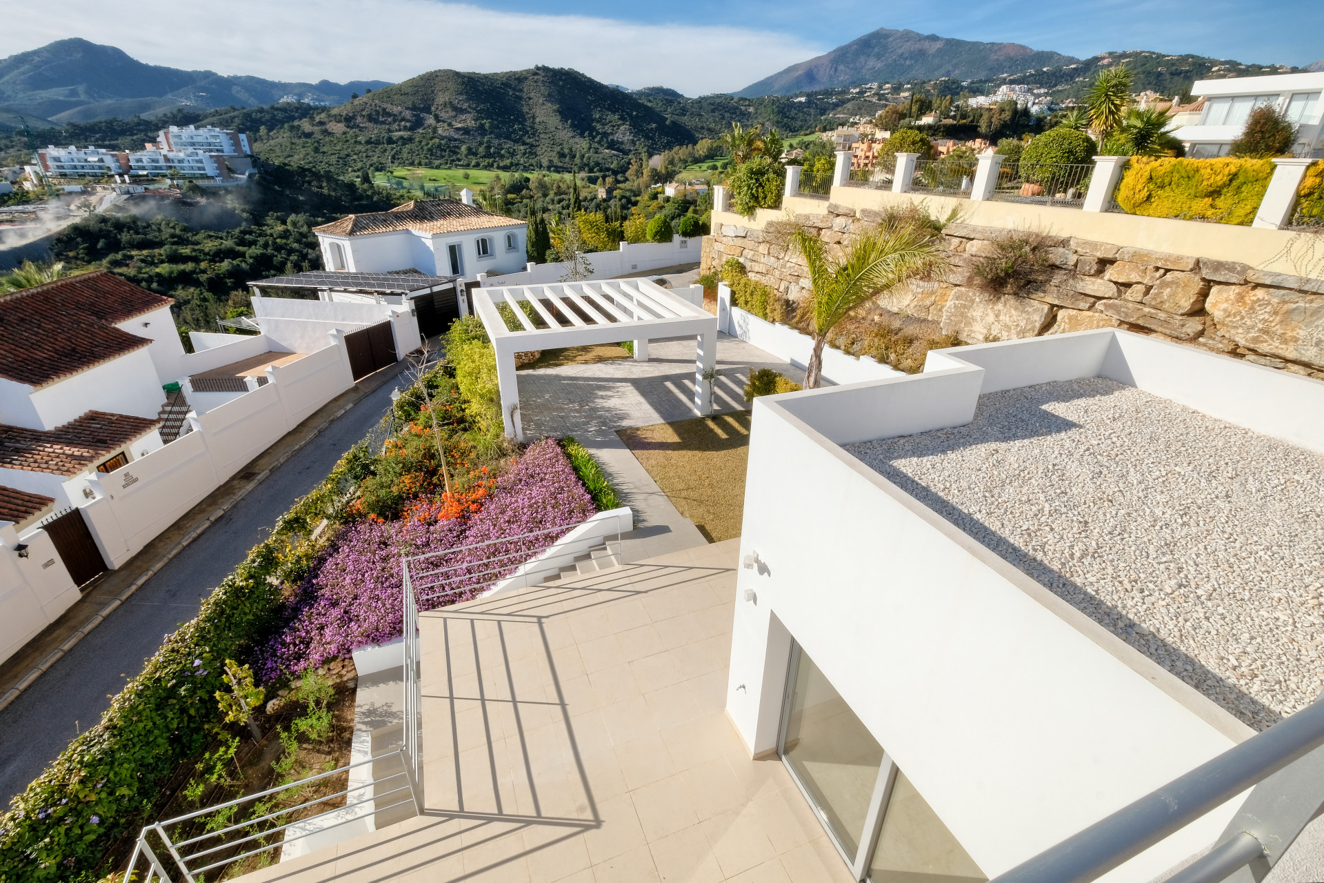 Overhead view of exterior stairs and terraces, with a white pergola and flowering plants below.