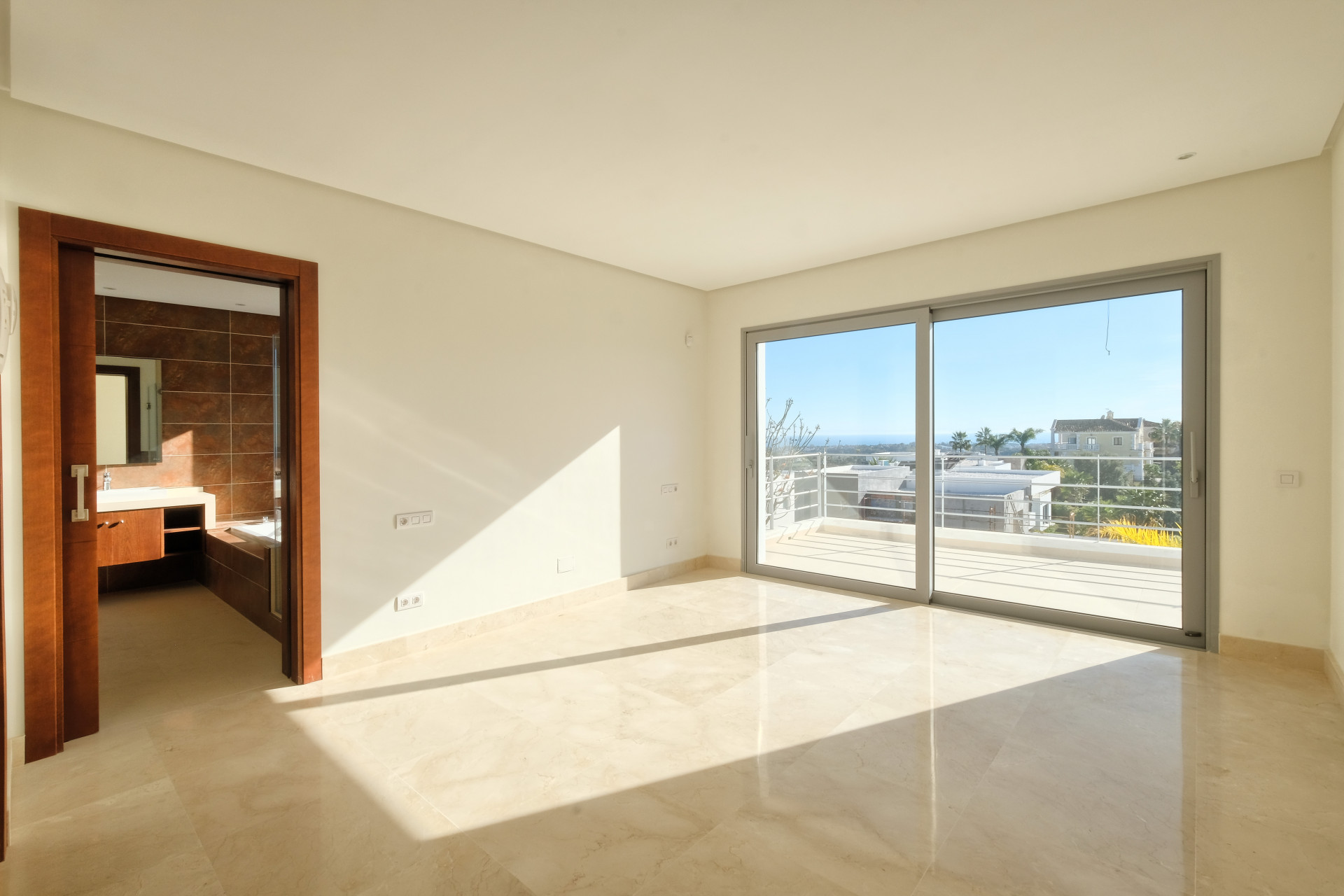 Bedroom with marble floors and a large sliding glass door opening to a balcony. An ensuite bathroom is visible.