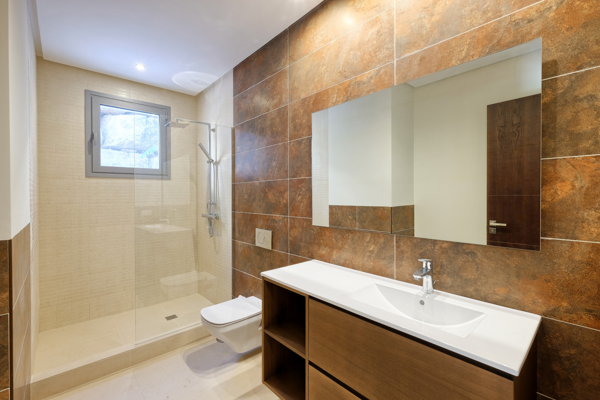 Bathroom with a glass shower enclosure, large mirror, and vanity with a white basin. Brown tiled walls.