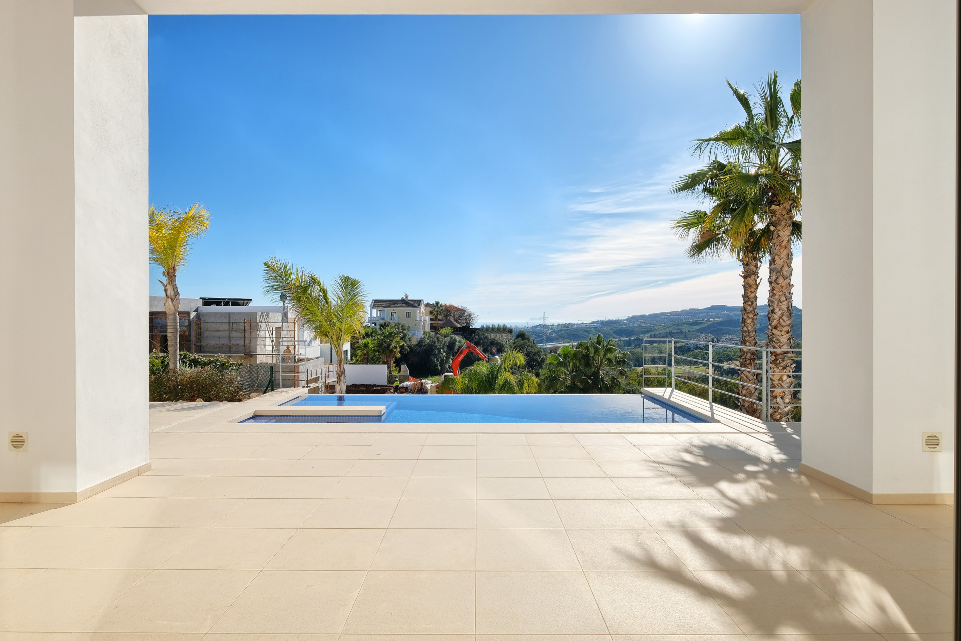 Patio with infinity pool, mountain views, and palm trees under a blue sky.
