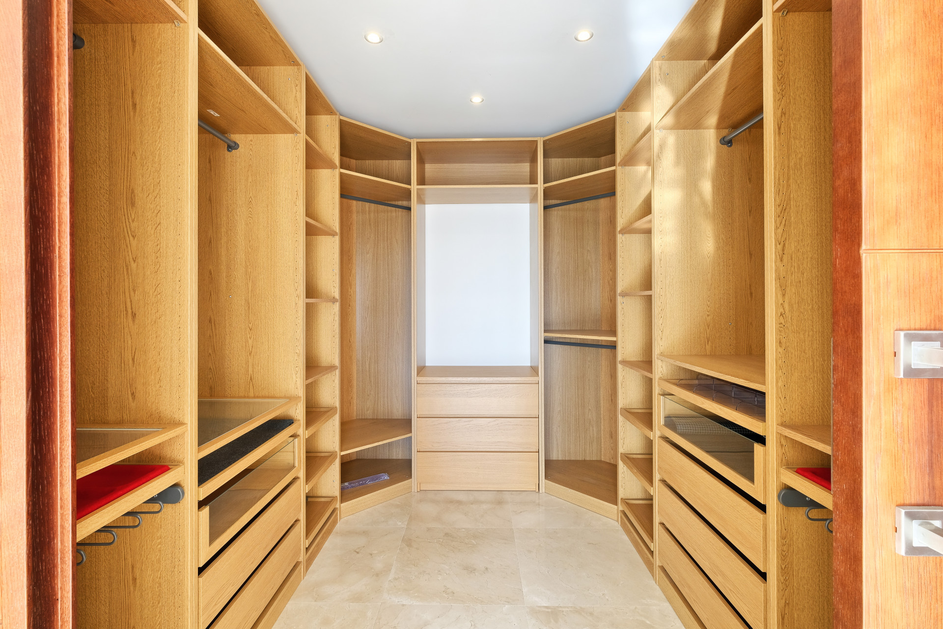 Walk-in closet with light wood shelving units, drawers, and hanging rods arranged in a U-shape.
