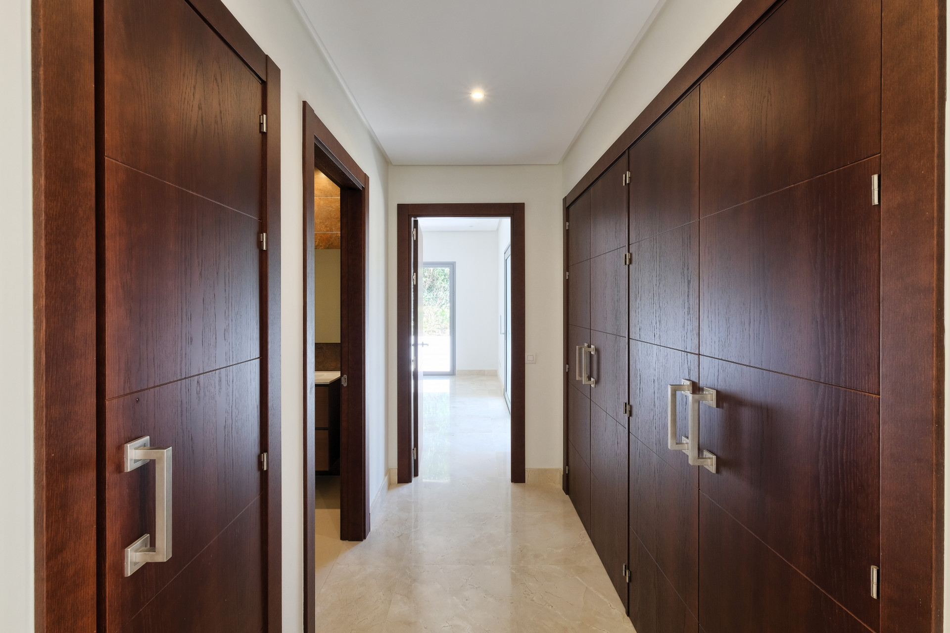 Indoor hallway with dark wood doors, recessed lighting, and a light-colored tiled floor.