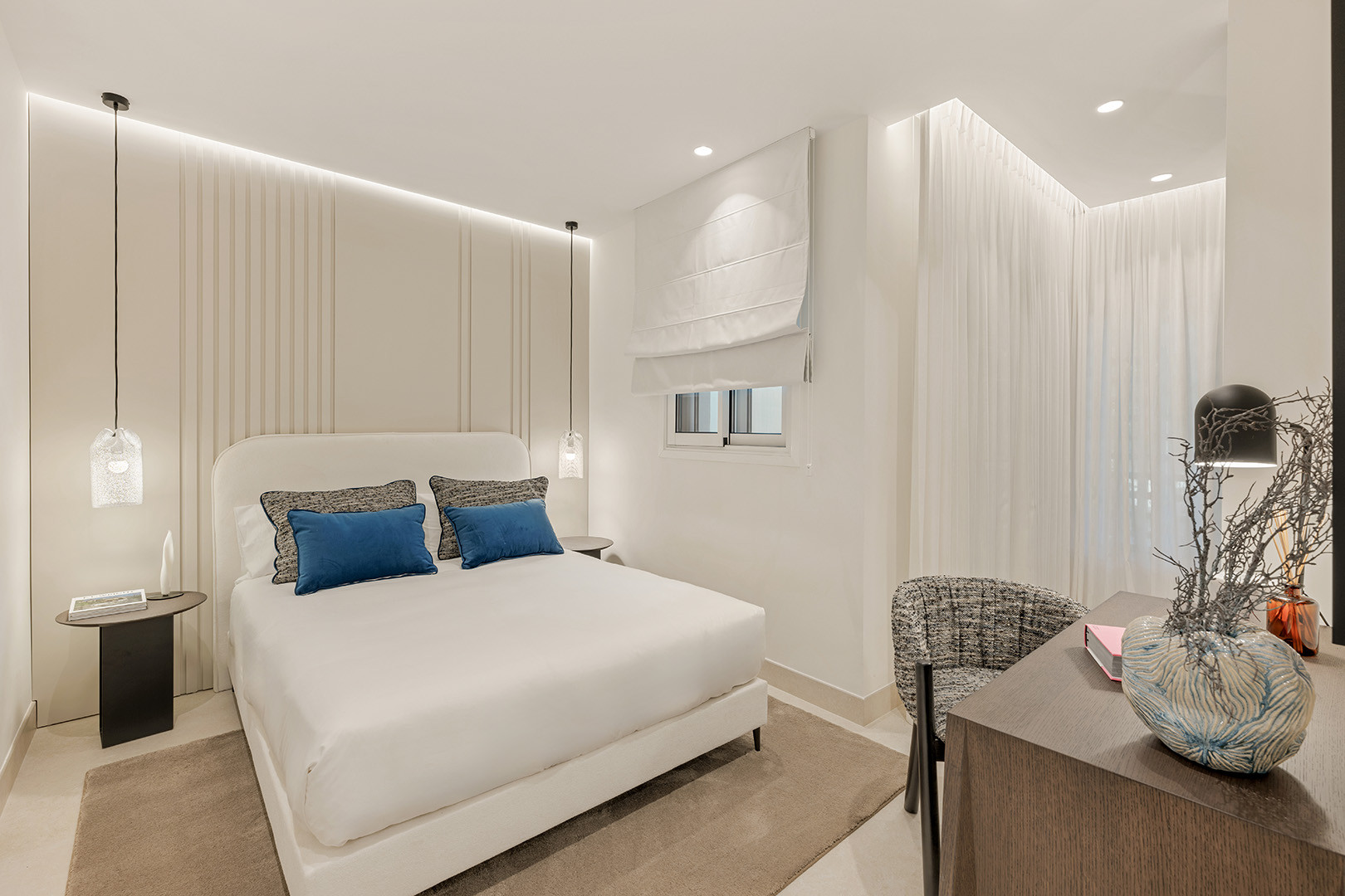 Bedroom with white bed, blue pillows, pendant lights, and a small desk area with a chair.