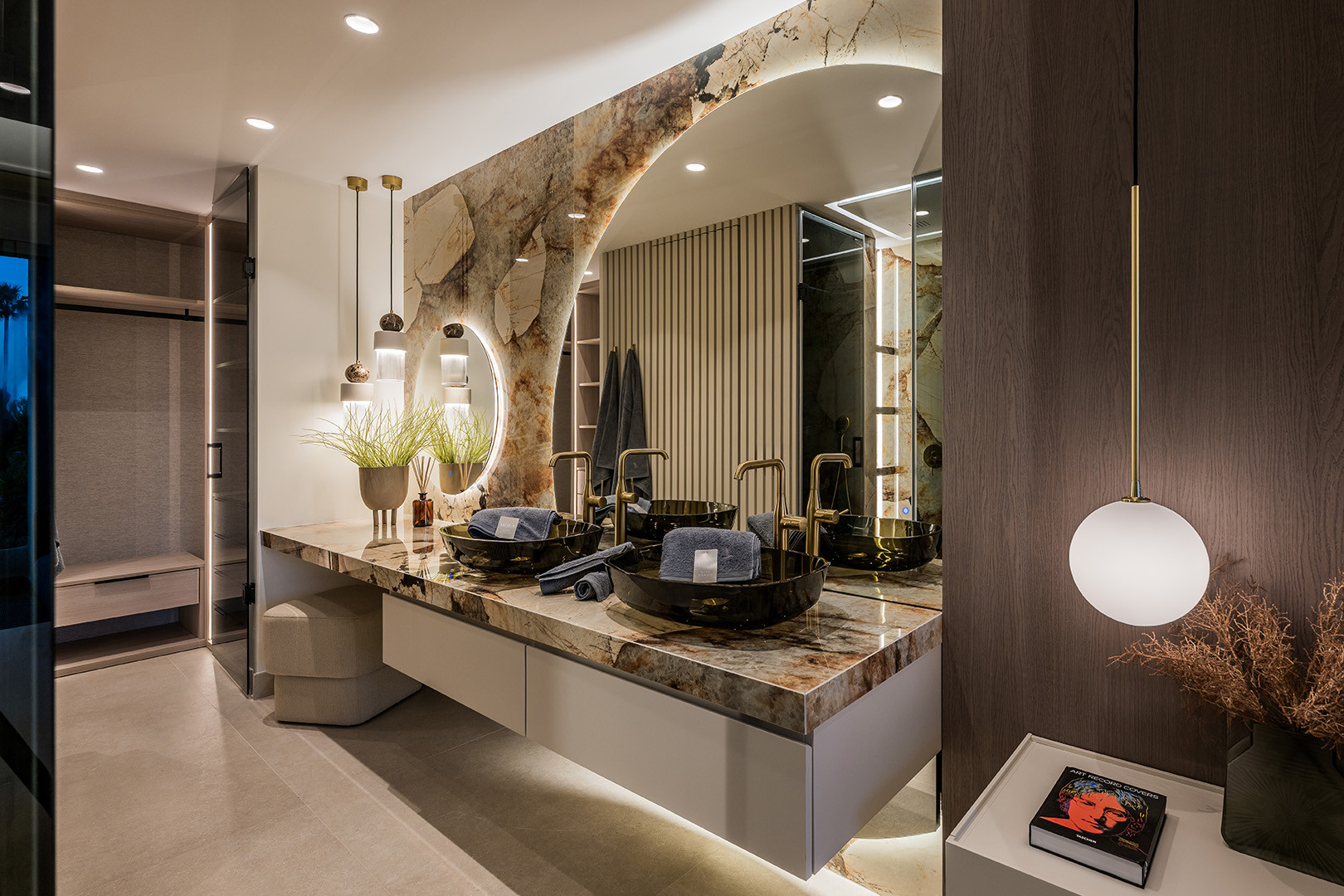 Wide shot of a bathroom vanity with two black sinks, gold faucets, and multiple light fixtures. Open closet to the left.