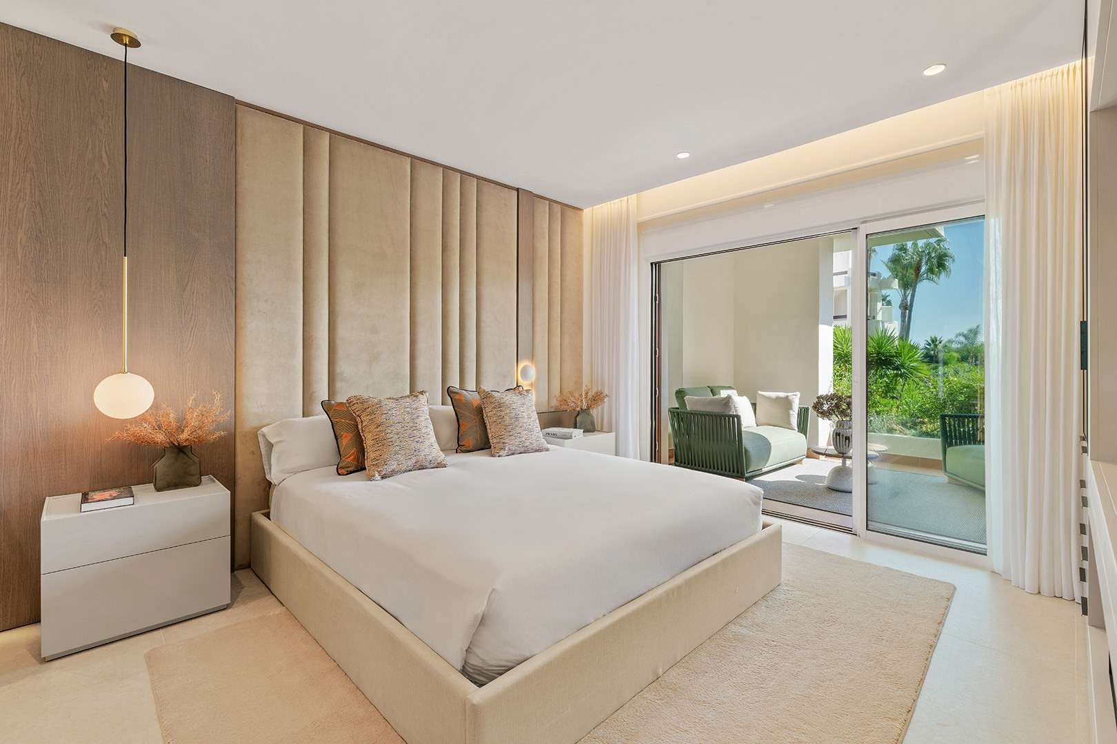 Bedroom with a large bed, upholstered headboard, and sliding glass doors leading to a balcony.
