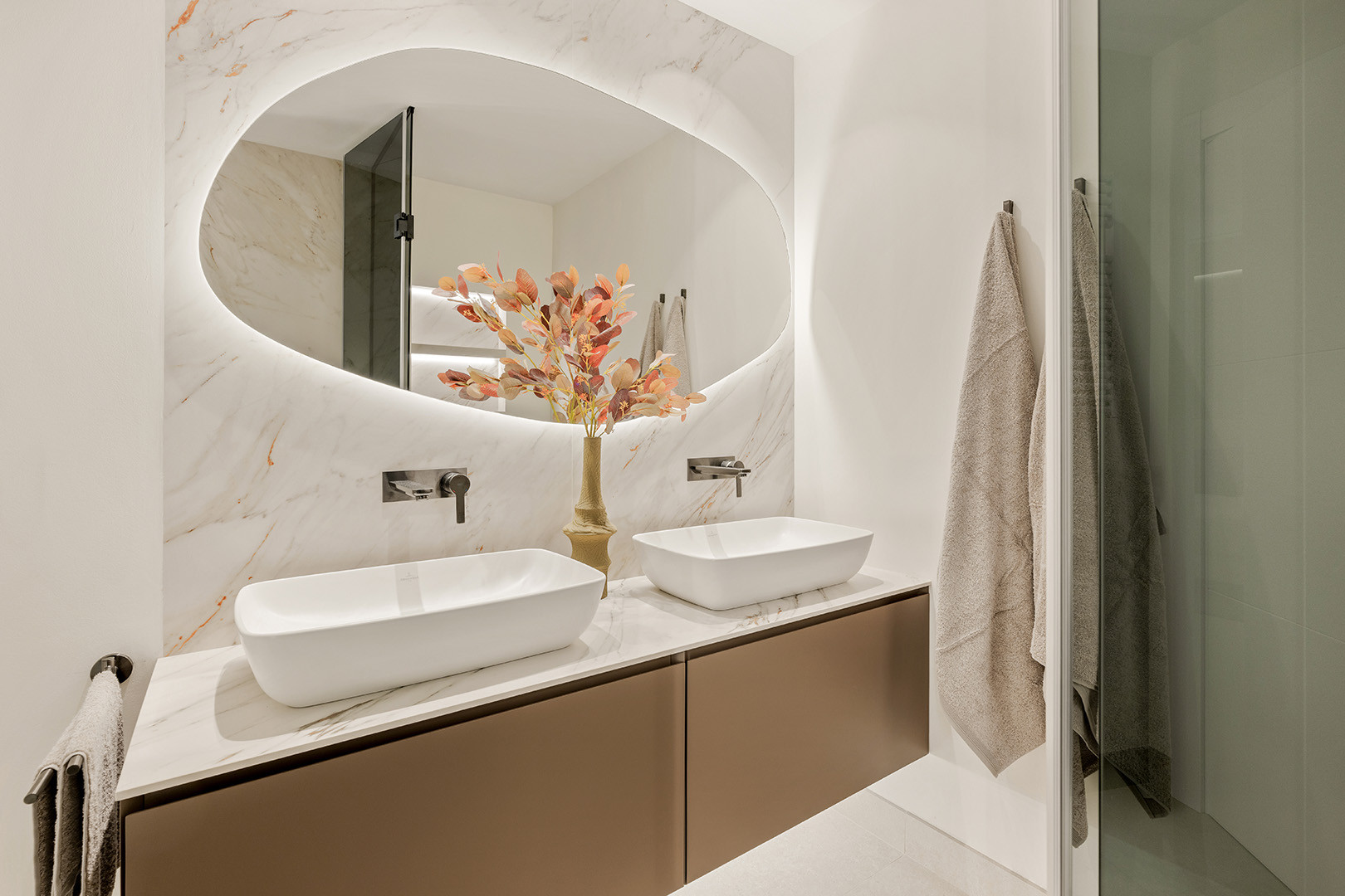 Bathroom vanity with two white sinks, a back-lit mirror, and marble-effect backsplash.