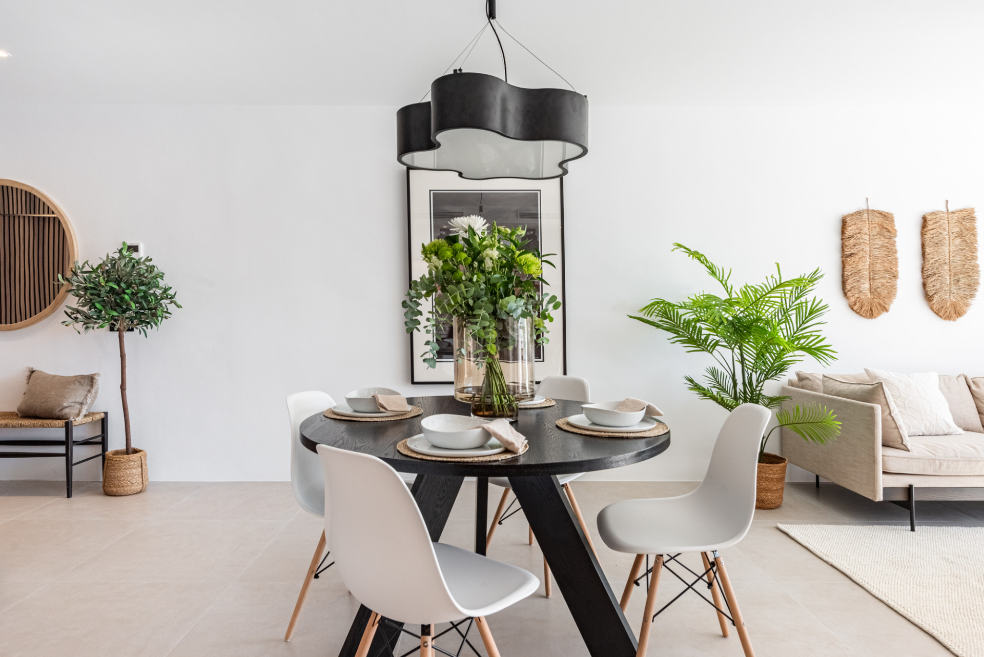 Dining area with black round table set for four, black pendant lights, and a large plant next to it.