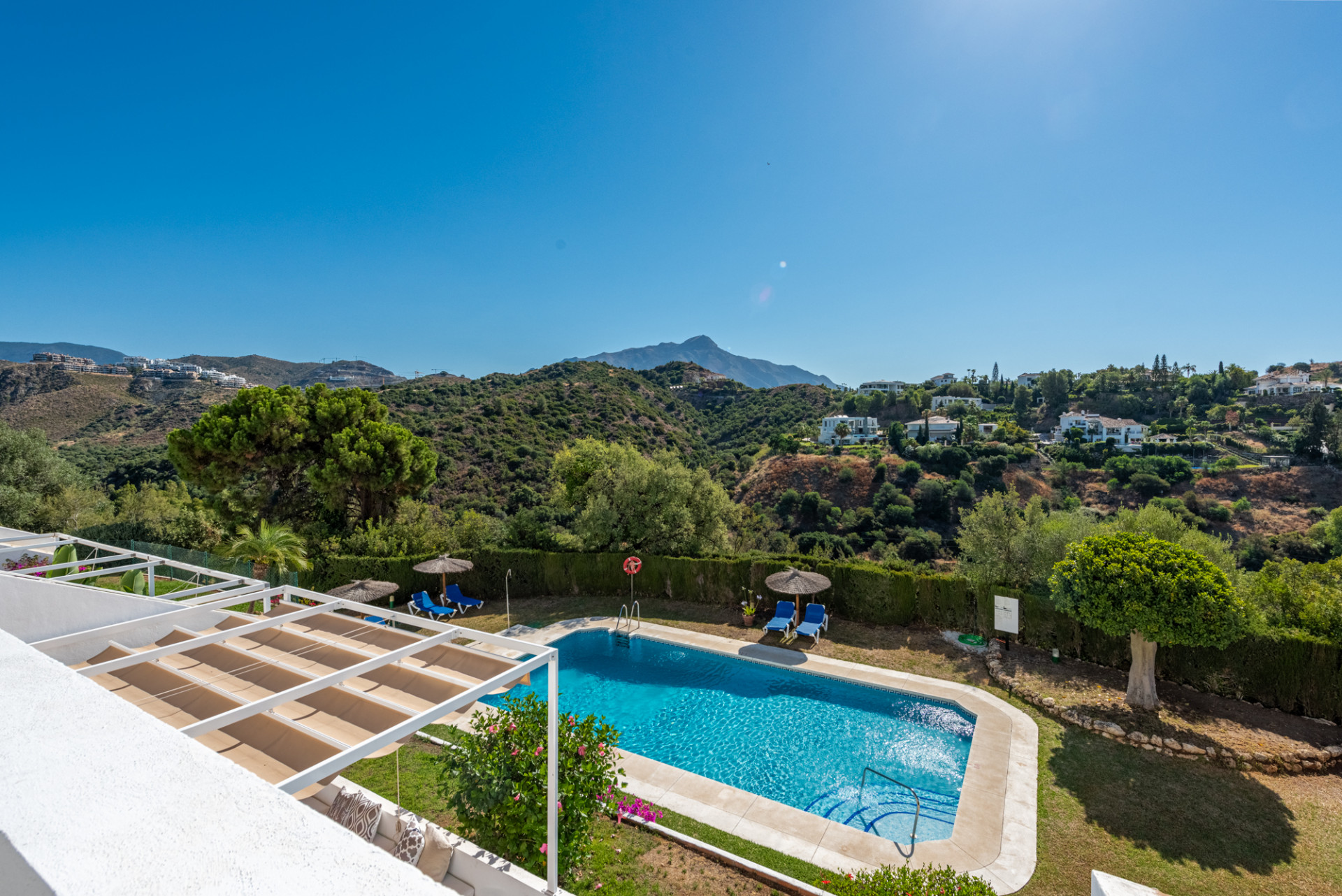 Panoramic view from above a pool area, showing distant mountains, green hills, and white residential buildings.