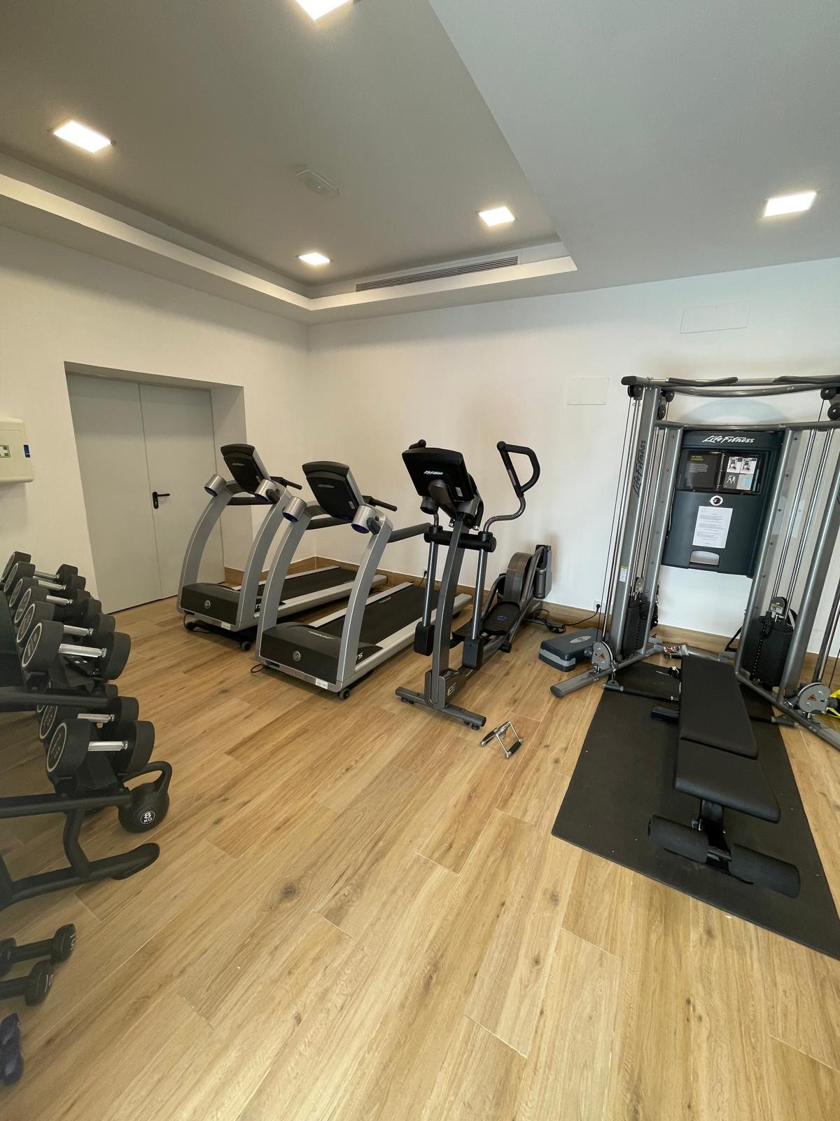 Fitness room with treadmills and weights arranged along the walls.