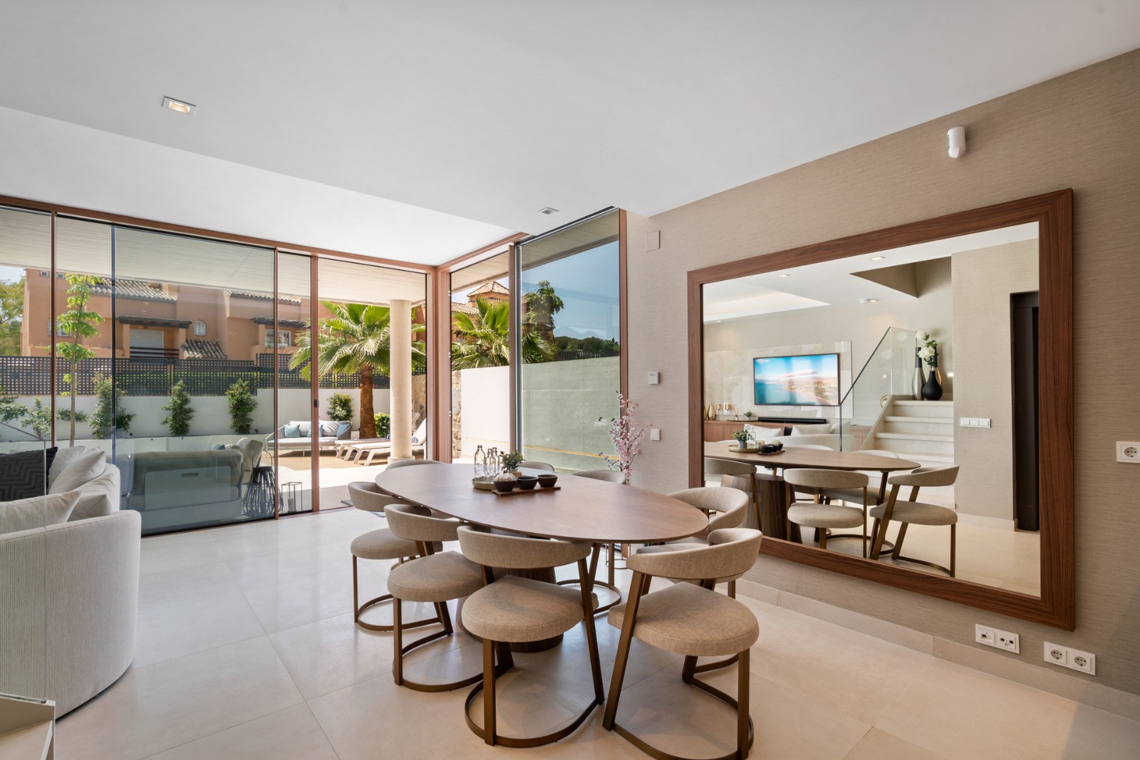 Dining area with a large mirror reflecting the living space, showing a modern aesthetic and light fittings.