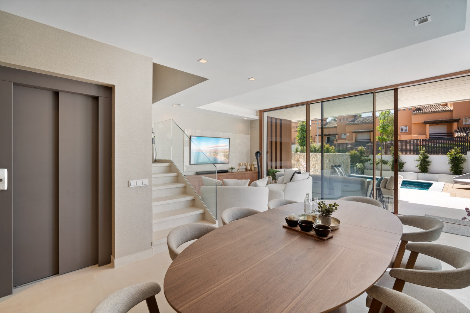 Dining room view towards the outdoor pool area, with large glass doors and light-colored furniture.