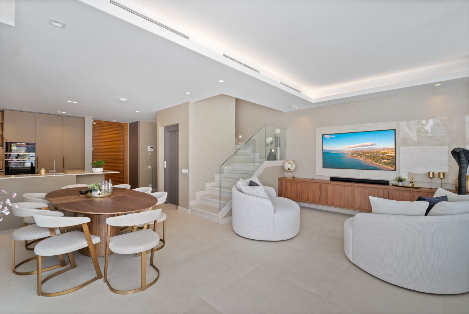 Living area with a round dining table and modern furniture, featuring a TV screen on the wall.