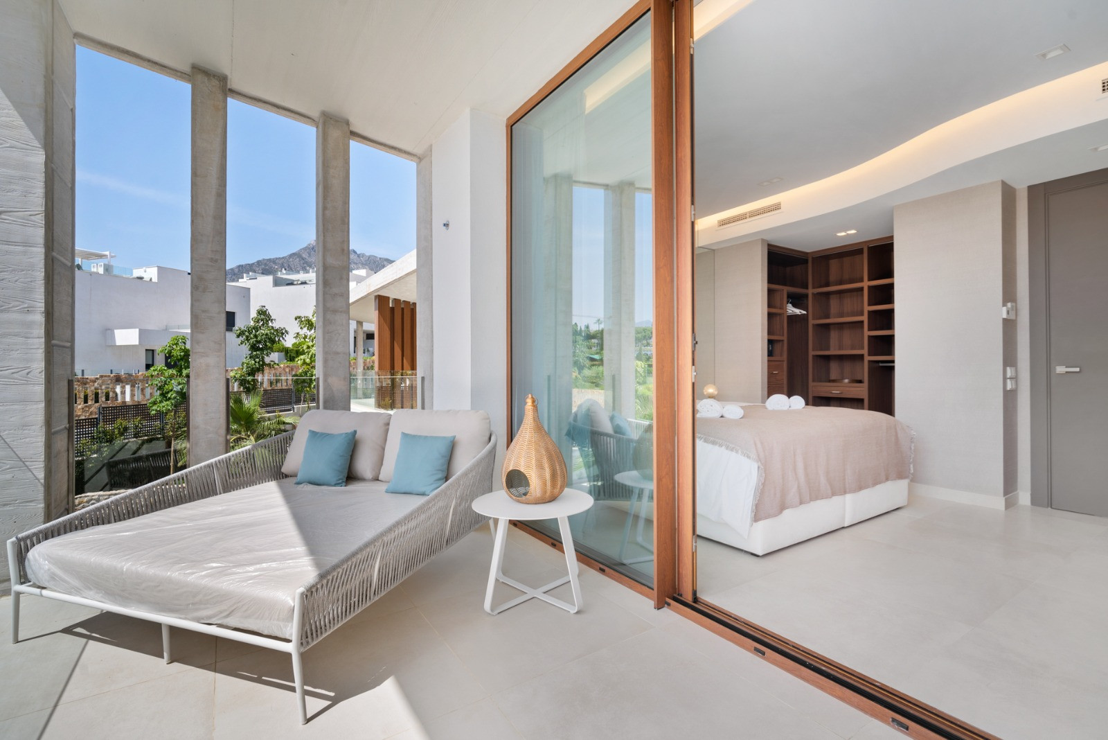 Outdoor lounge area with daybed, stone columns, and views of nearby mountains and greenery.