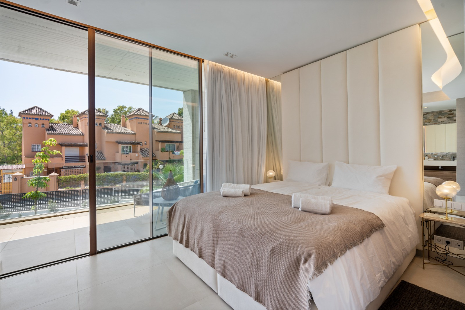 Bedroom with large windows, plush bedding, and views of neighboring architecture.