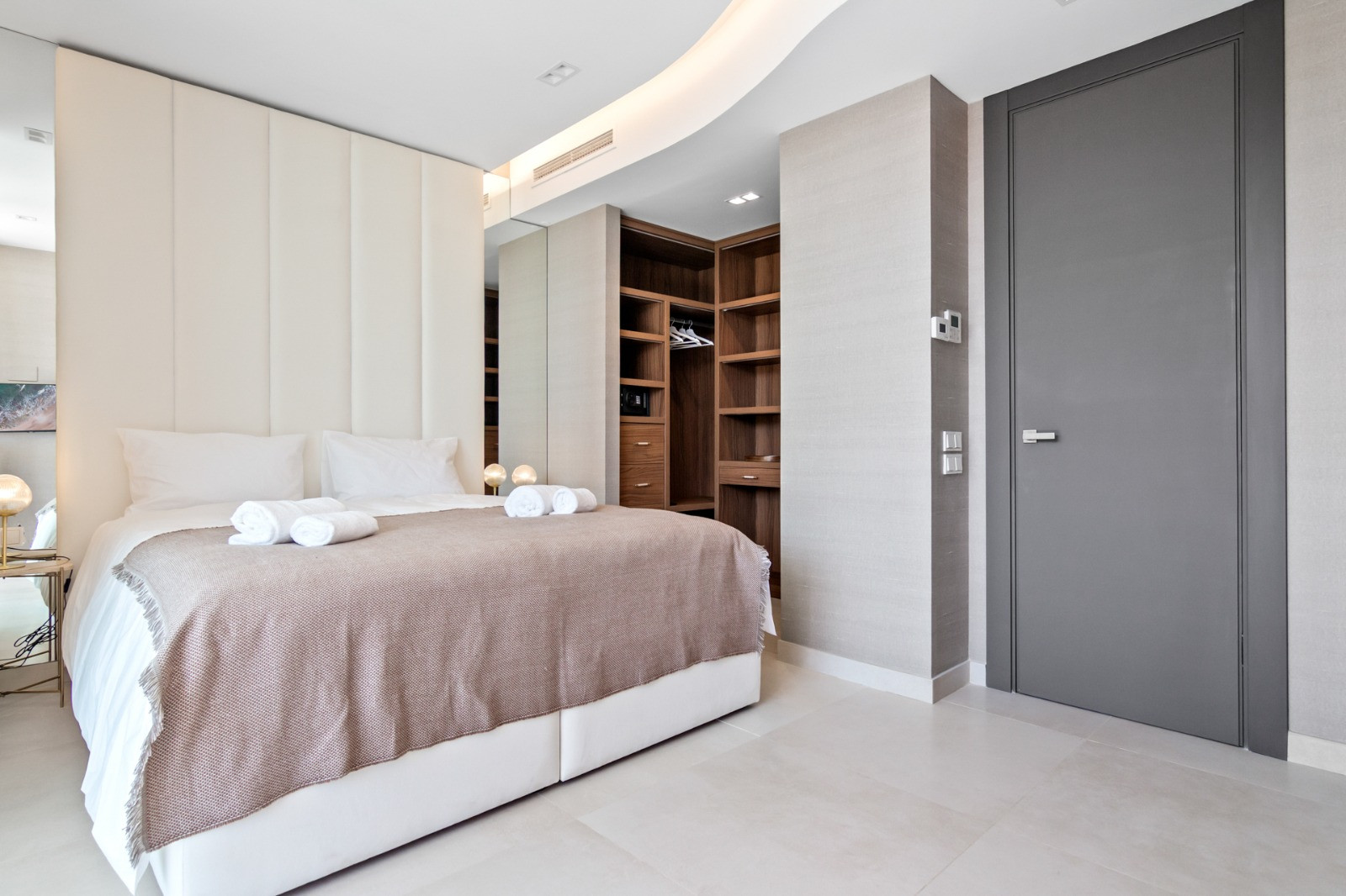 Light-filled bedroom featuring a bed with decorative linens and mirrored wall cabinets.