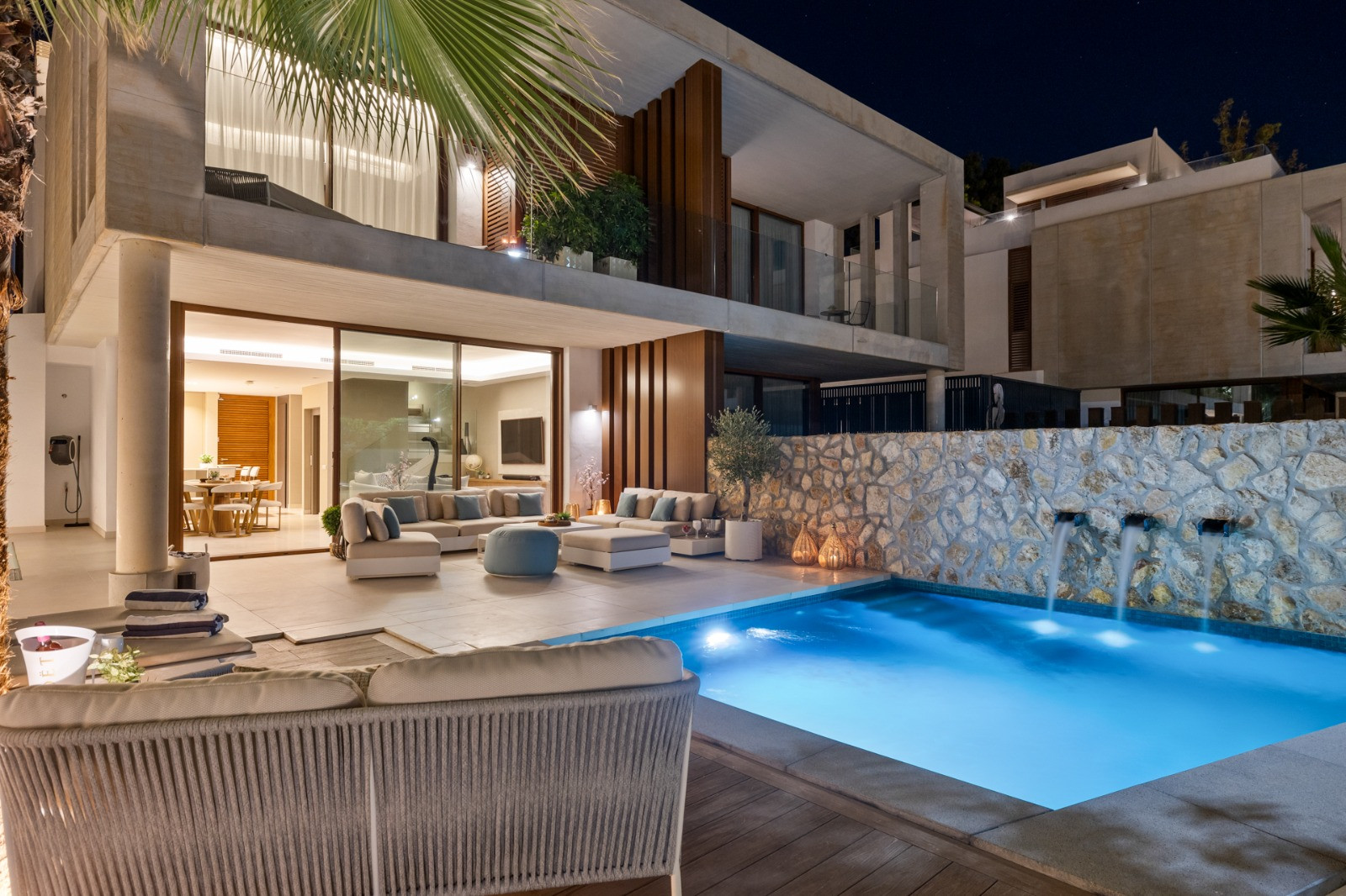 Night view of a modern house with a pool, outdoor seating, and stone wall features, showcasing architectural design.