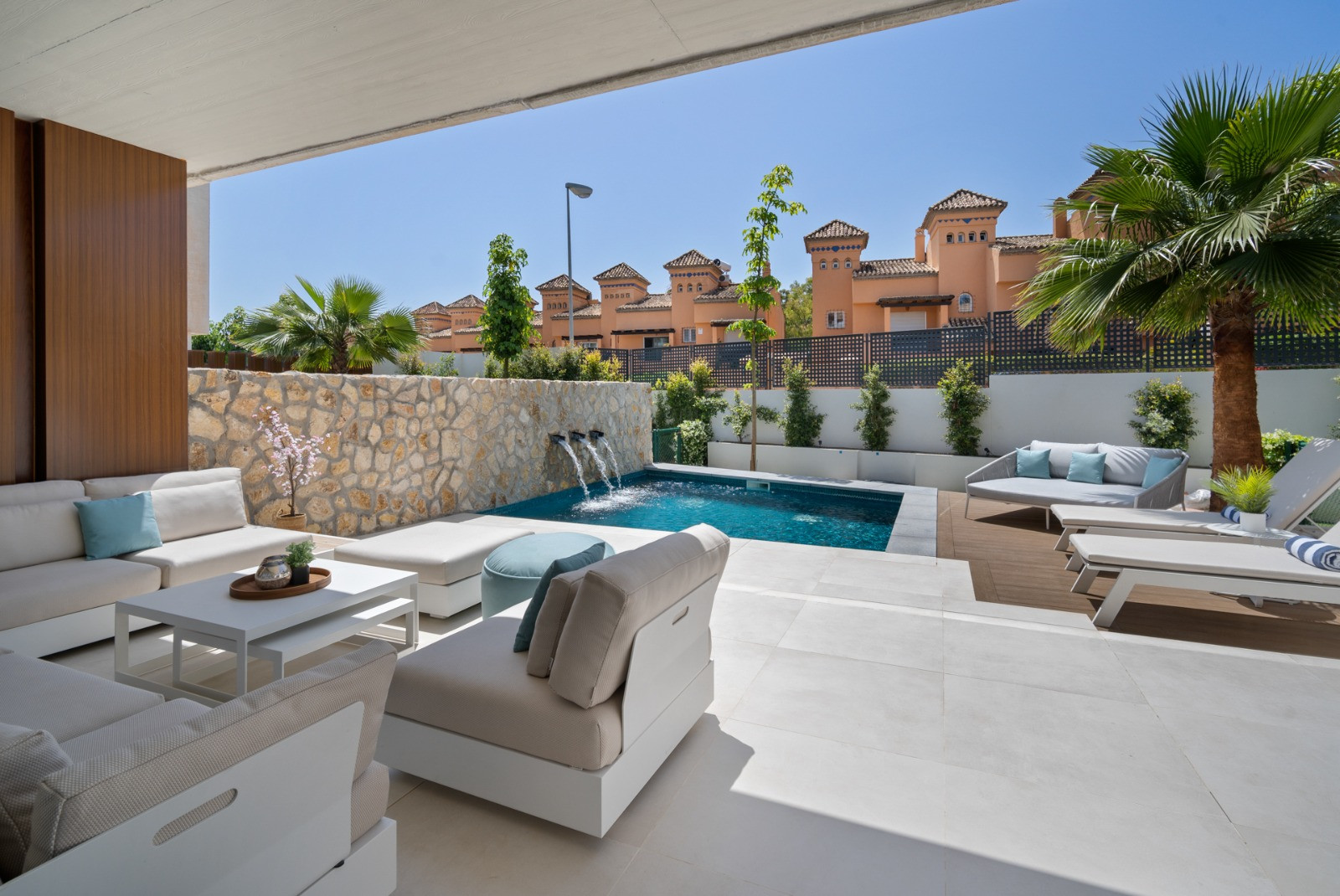 View of the pool and garden from a shaded seating area.