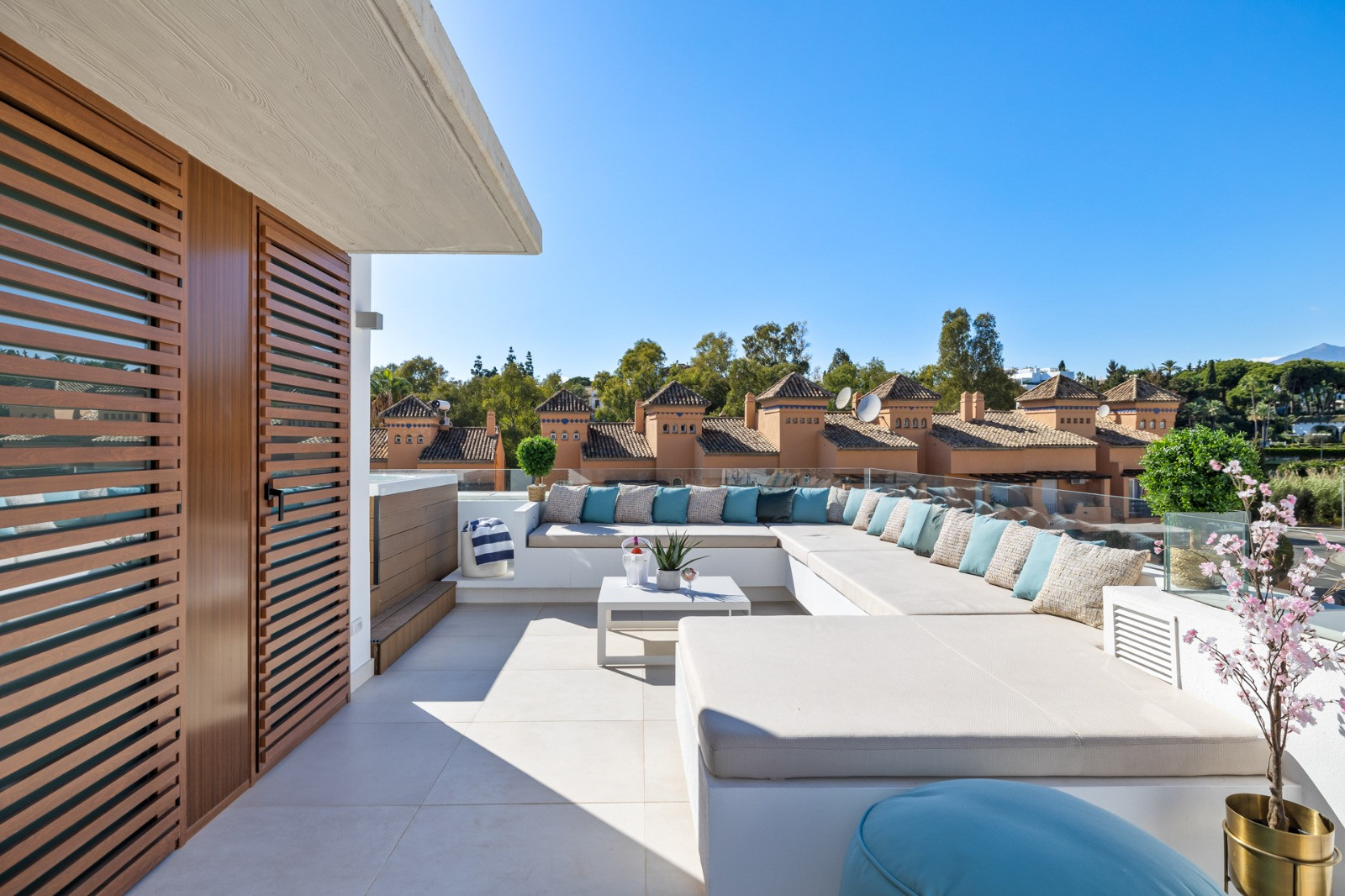 Outdoor lounge area featuring a large sectional sofa, decorative pillows, and greenery visible in the background.