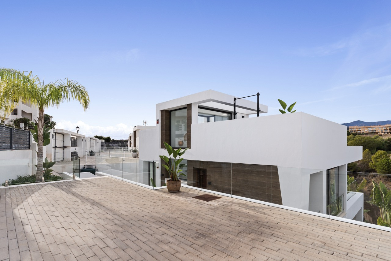 Exterior view showing a modern house with a terrace and surrounding plants under a clear sky.
