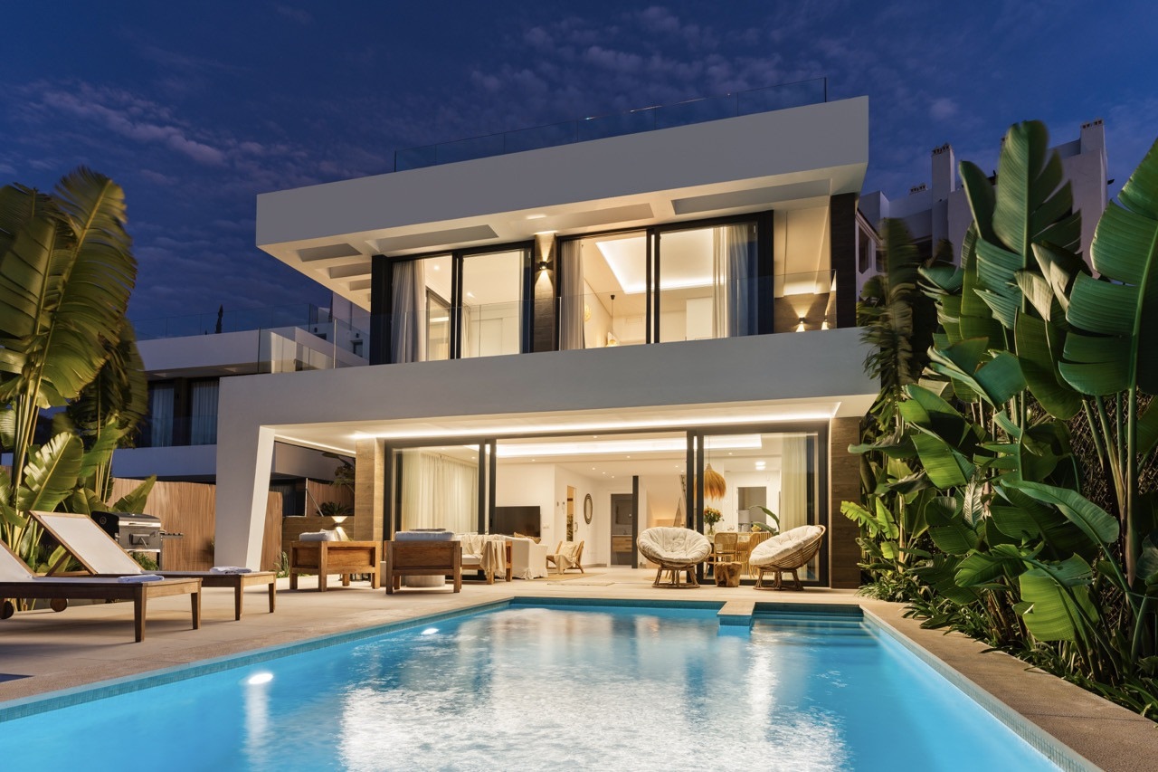 Modern house with a pool, surrounded by greenery and palm trees at night.