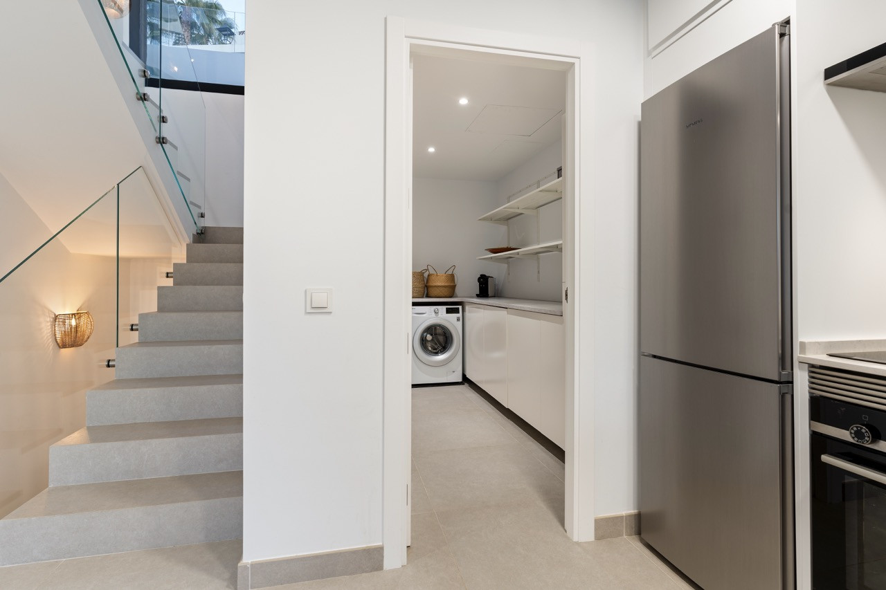 Laundry area with washing machine and shelves, adjacent to stairs leading up.