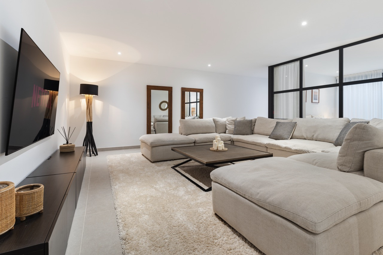 Spacious living room with large sectional sofa and flat-screen TV on wall.