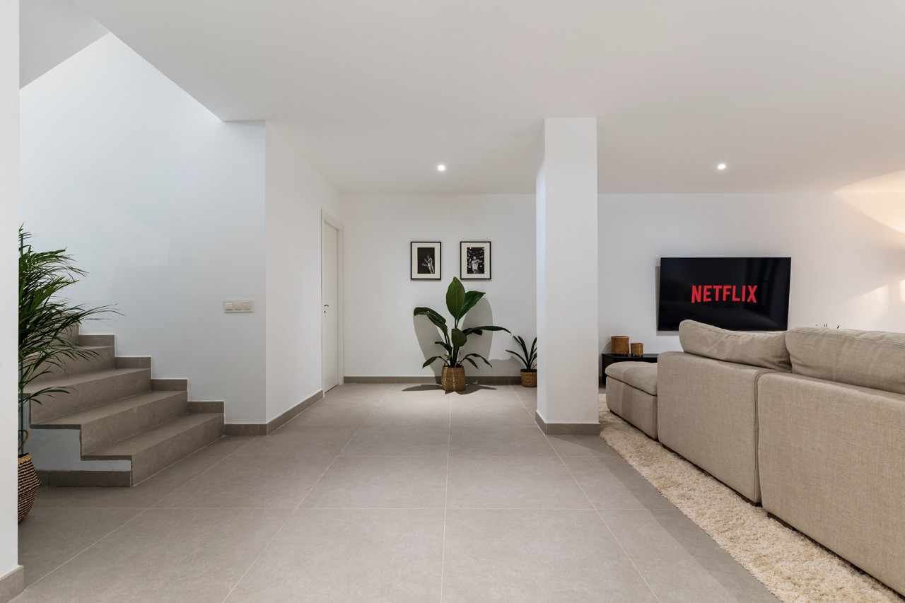 Cozy living area with a large sofa and a TV on the wall, accompanied by indoor plants.