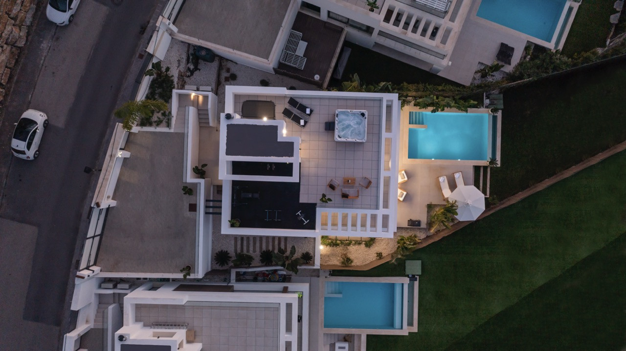 Aerial view of the property featuring a jacuzzi, terrace seating, and pools highlighted at dusk.