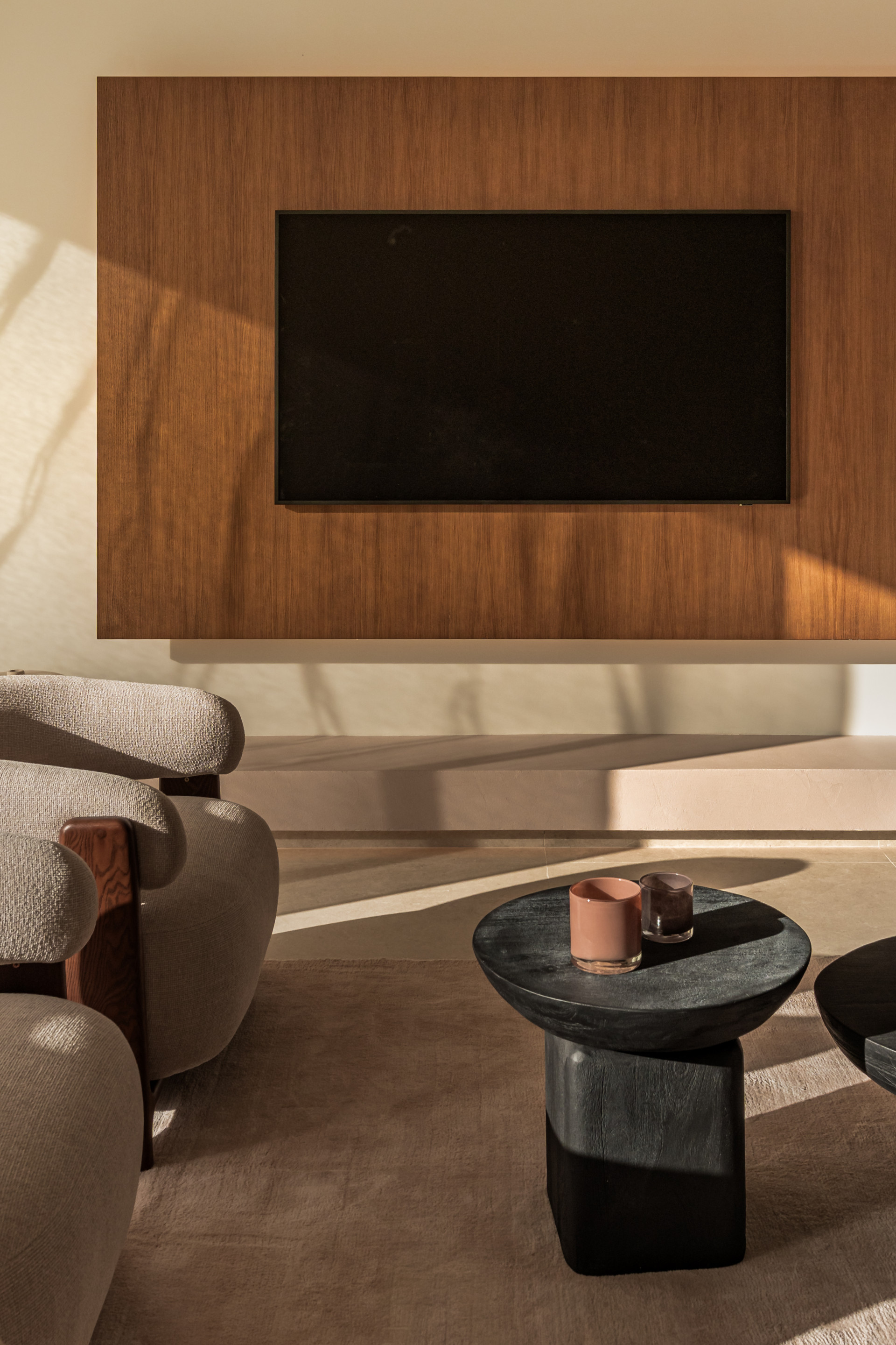 Close up of a living room corner with an armchair, coffee table, and a wall-mounted TV on a wood panel.