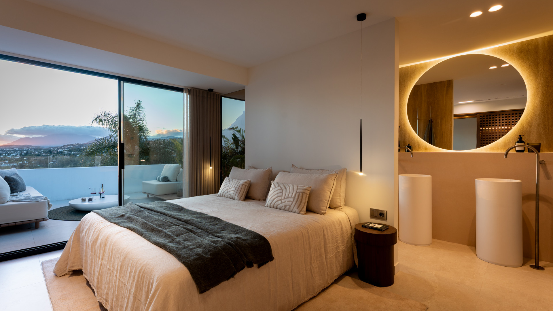 Bedroom with a large bed, private balcony, and integrated bathroom vanity with round mirror.