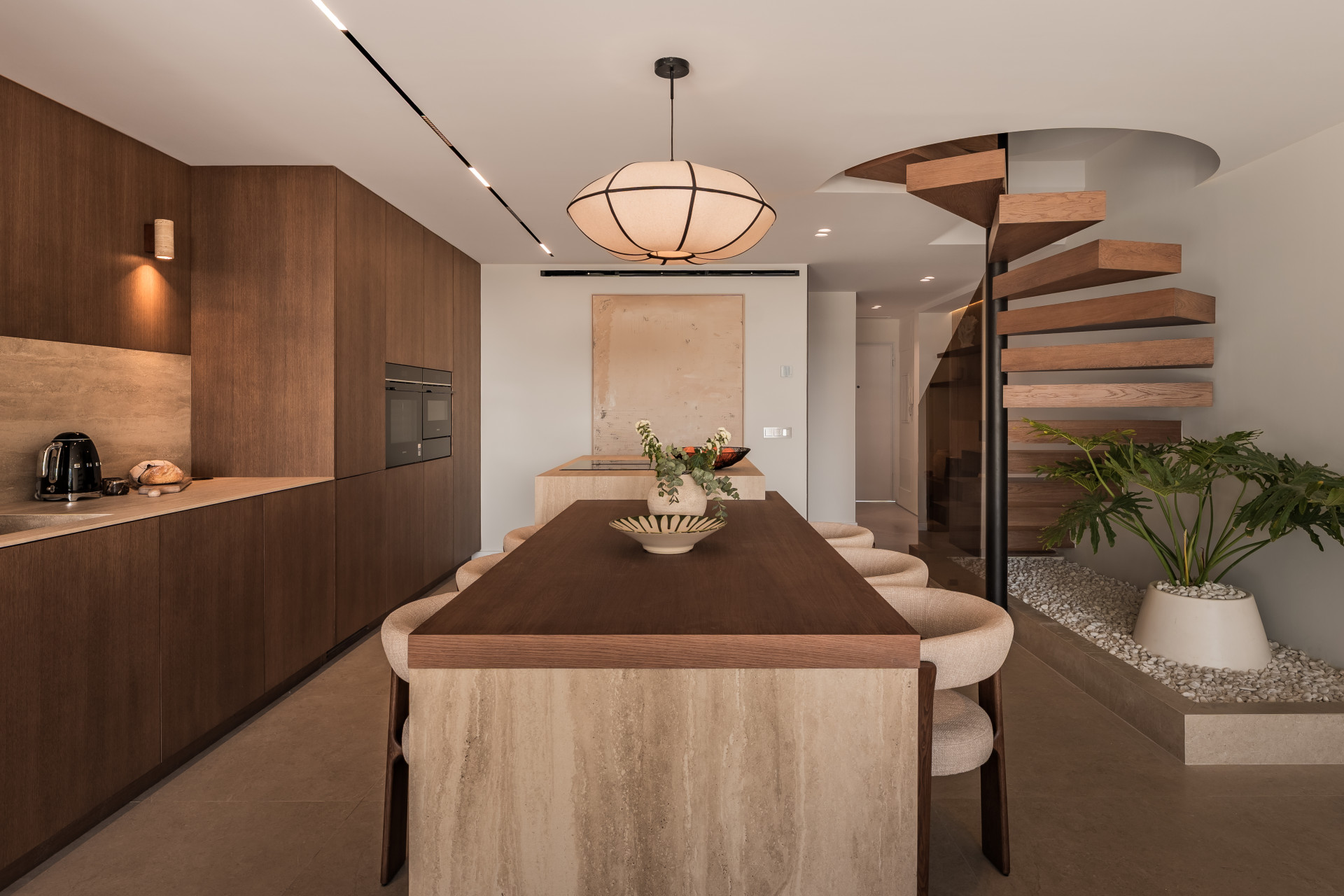 Modern kitchen with wood cabinetry and dining island, next to a spiral staircase.
