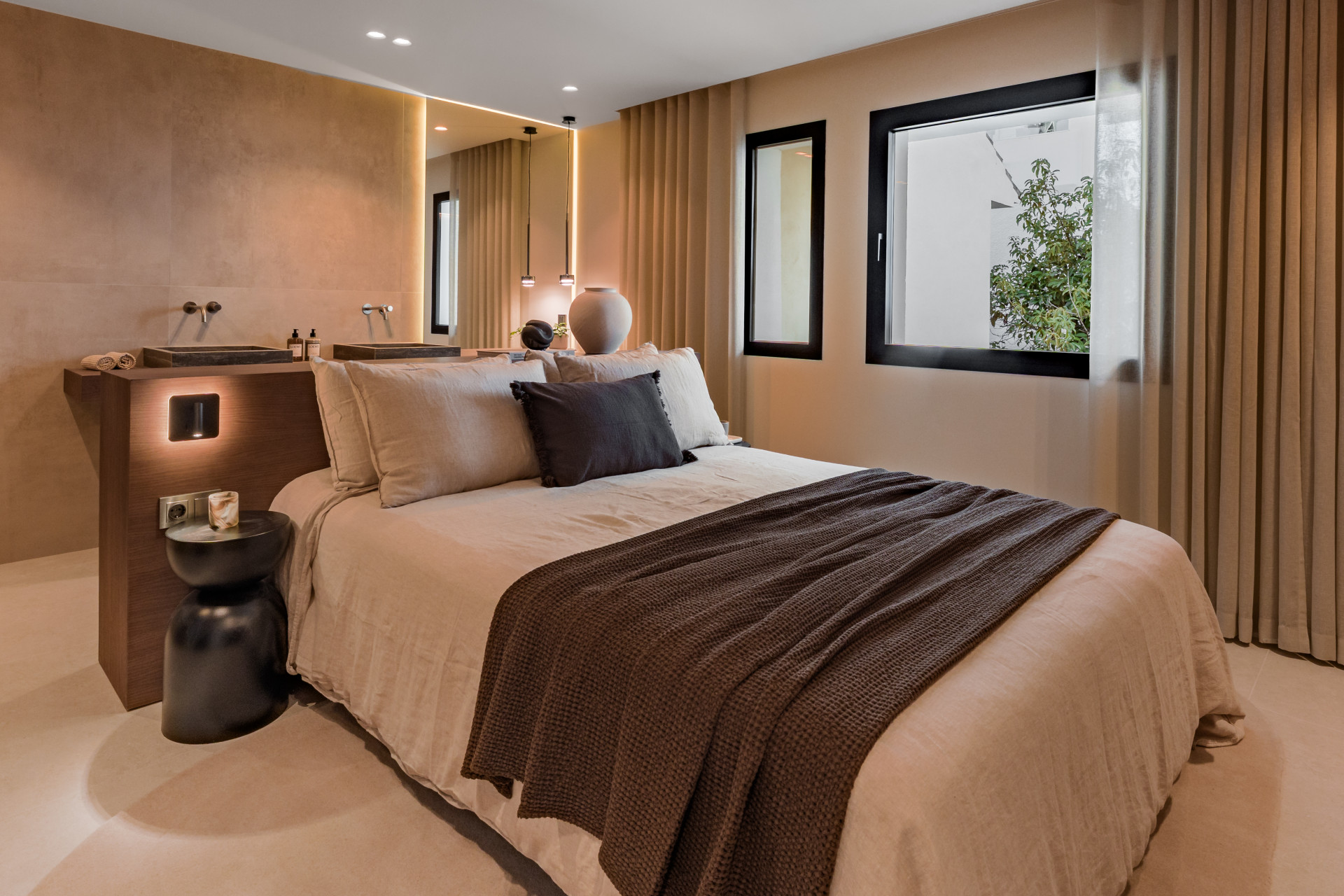 Bedroom with a large bed, two windows, and an integrated bathroom vanity with a black stone sink.