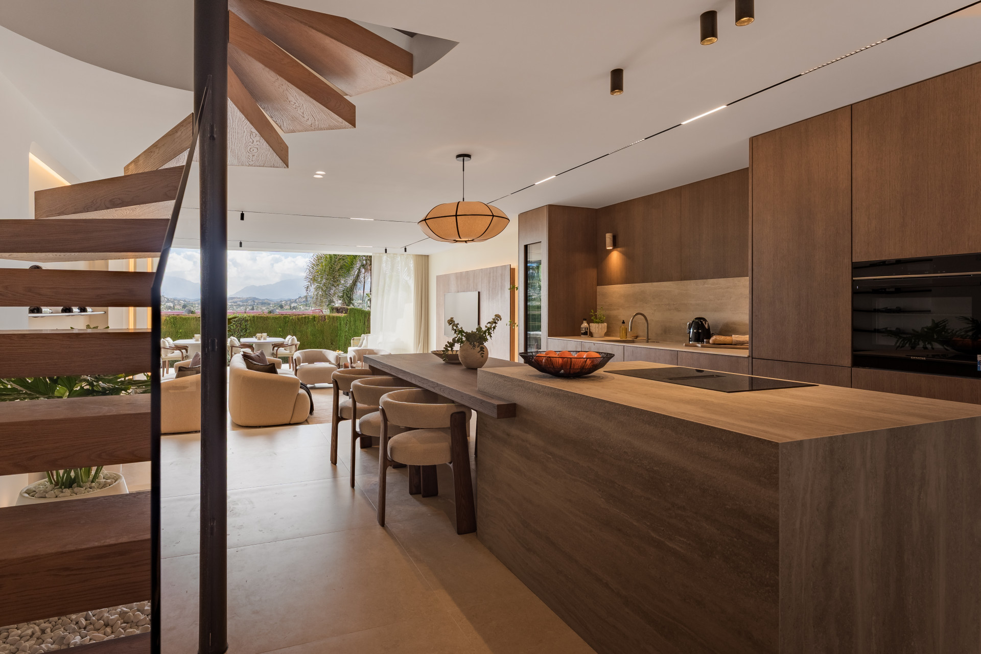 Kitchen with a large island and spiral staircase, overlooking an outdoor living area and mountains.